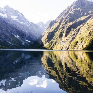 Lake Marian Track wandern, bei Marian Falls im Fiordland National Park Südinsel Neuseelands, Wanderung zum See Marian, Lake Marian, Tal, hanging valley, schneebedeckte Gipfel in der Ferne, Berge spiegeln sich im klaren Wasser, schönes Licht, Sonne, Steine