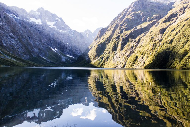 Lake Marian Track wandern, bei Marian Falls im Fiordland National Park Südinsel Neuseelands, Wanderung zum See Marian, Lake Marian, Tal, hanging valley, schneebedeckte Gipfel in der Ferne, Berge spiegeln sich im klaren Wasser, schönes Licht, Sonne, Steine