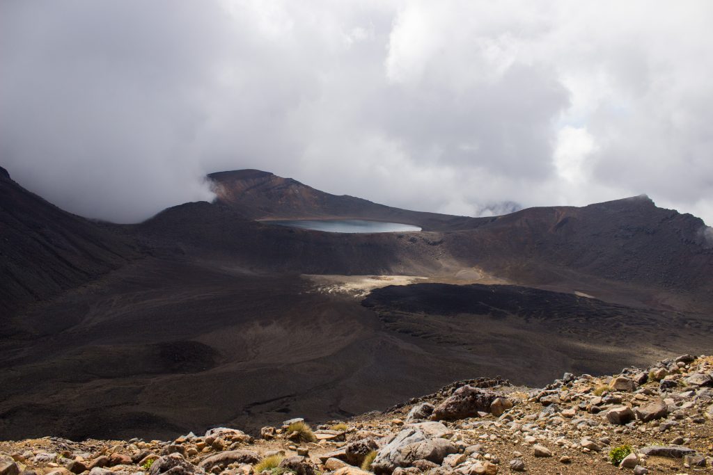 Tongariro Alpine Crossing Wanderung, Nordinsel Neuseeland, Vulkanlandschaft, lebensfeindliche Landschaft, in Wolken gehüllte Berge, Geröll und Steine, Aussicht auf Bergsee in Ferne