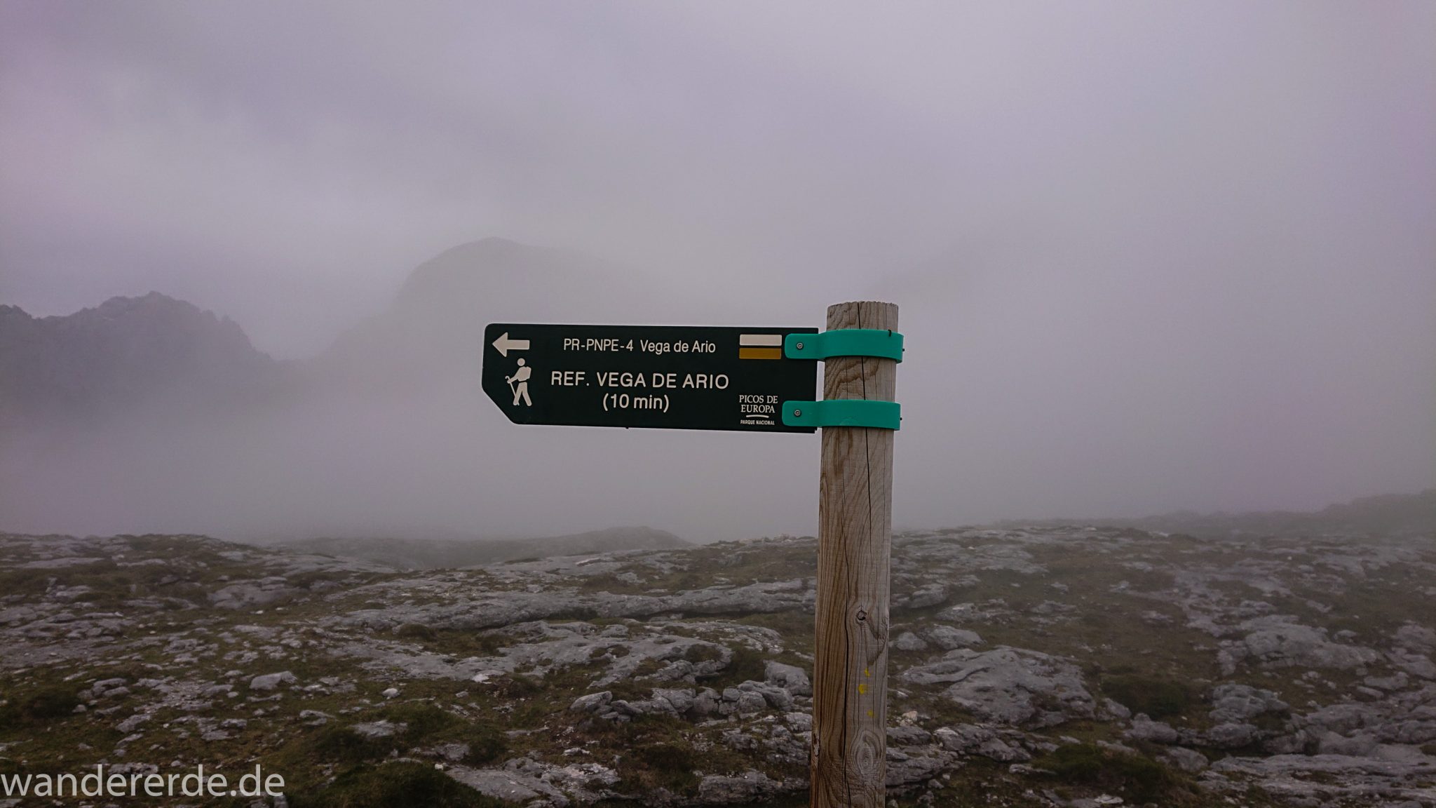 Wanderung Vega de Ario Picos de Europa Spanien, Wegweiser Schild PR-PNPE-4 Refugio Vega de Ario, dichte Wolken, Bergregion in Nordspanien, Wandern, grüne Wiesen, zerklüftete Felsen, Steine