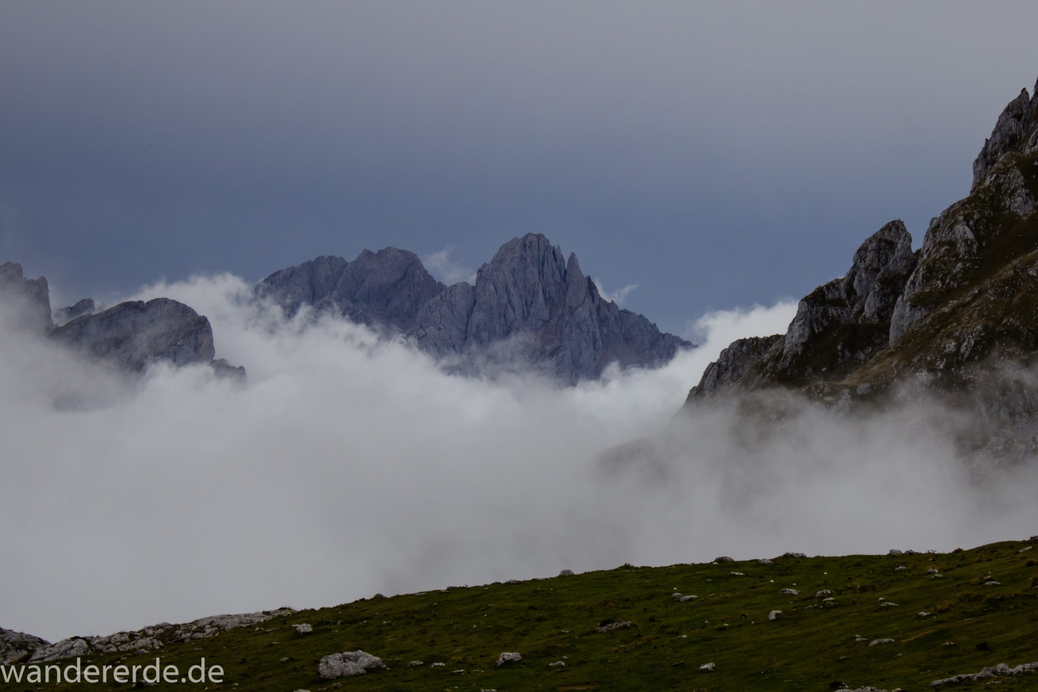 Wanderung Vega de Ario Picos de Europa Spanien, dichte Wolken, Bergregion in Nordspanien, Wandern, zerklüftete Felsen, Steine, schmaler Wanderpfad, atmosphärisch, Aussicht auf große Bergkette, grüne Wiese, Wolken ziehen auf und verhüllen Berge, spitze Berggipfel