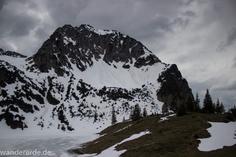 Wanderung Unterer Gaisalpsee, Wanderweg von Oberstdorf im Allgäu, Wanderpfad wird zunehmend schmaler, steil und felsig, weniger Bäume, Blick auf Allgäuer Berge mit Schnee und Unterer Gaisalpsee fast vollständig mit Eis und Schnee bedeckt, Wanderung zu Oberer Gaisalpsee nicht möglich Mitte Mai
