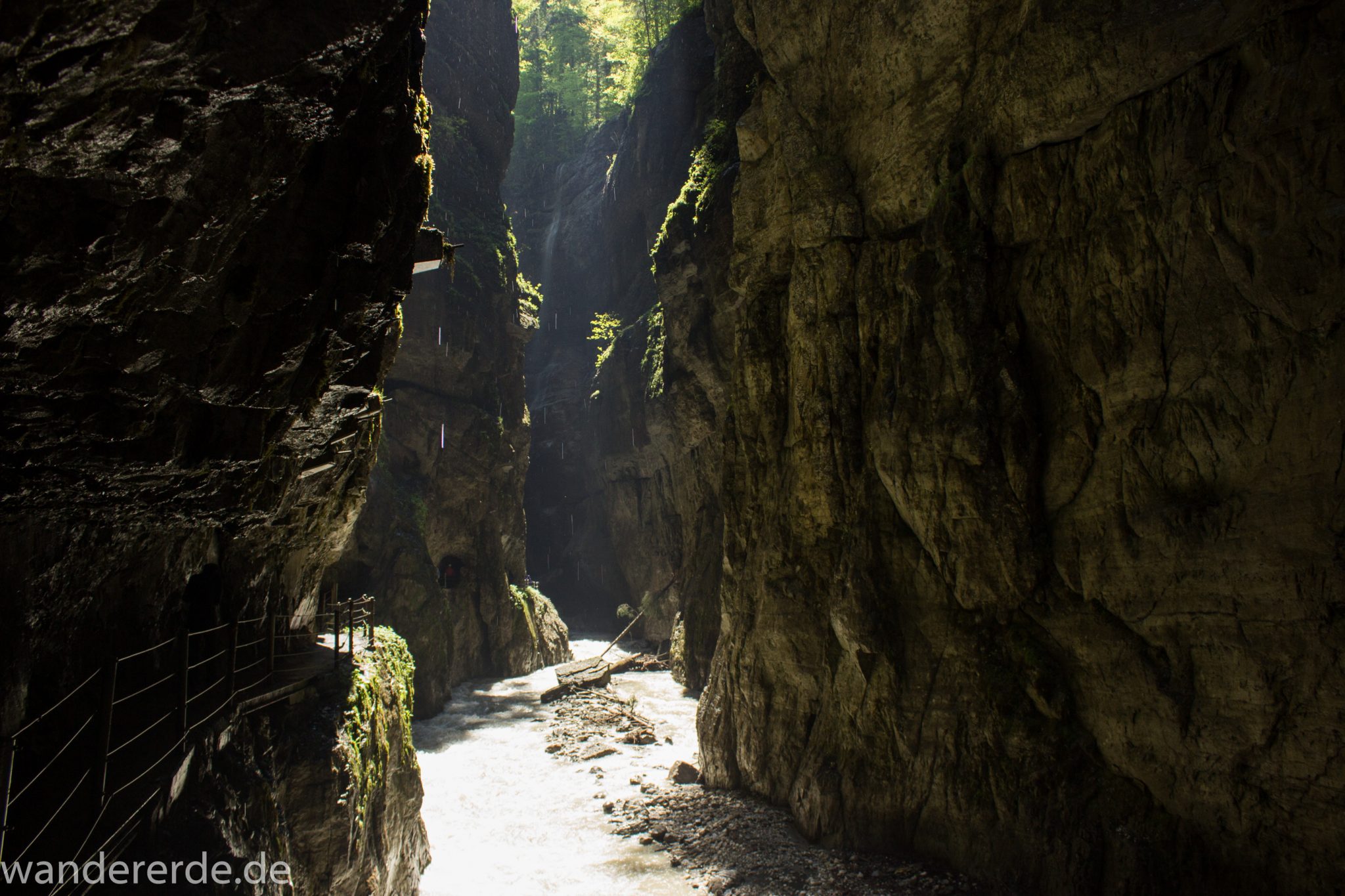 Rundwanderung Partnachklamm im Wettersteingebirge bei Garmisch-Partenkirchen, Bayern, steil aufragende Felswände, Licht strahlt von oben in die Klamm, gesicherter Wanderweg in den Fels gehauen, kühl und nass