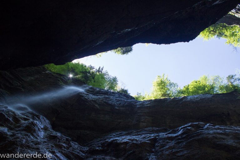 Rundwanderung Partnachklamm im Wettersteingebirge bei Garmisch-Partenkirchen, Bayern, steil aufragende Felswände, Licht strahlt von oben in die Klamm, kühl und nass, an Felswand bildet sich kleiner Wasserfall, oberhalb der Partnachklamm wächst schöner, dichter Wald