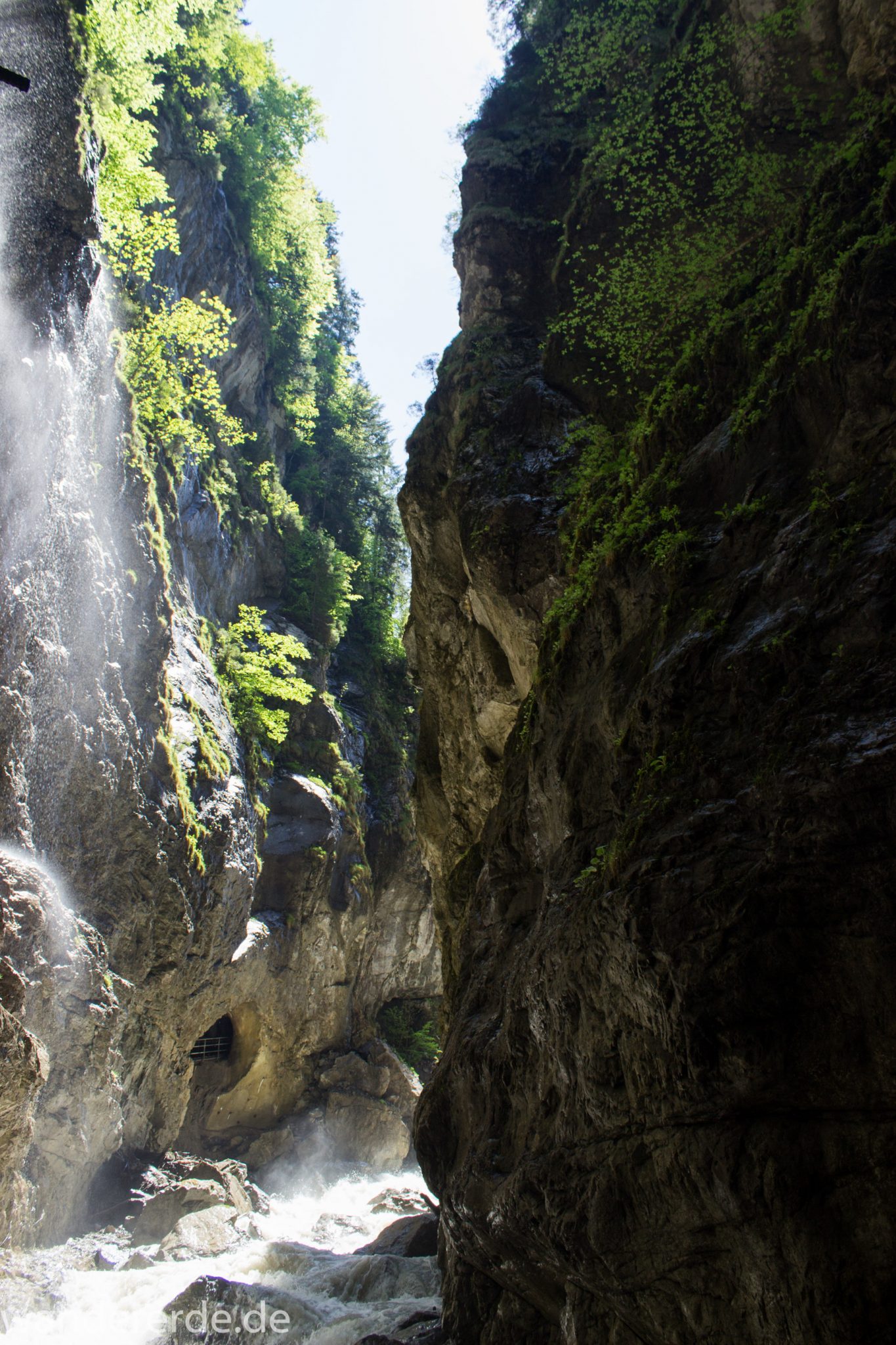 Rundwanderung Partnachklamm im Wettersteingebirge bei Garmisch-Partenkirchen, Bayern, steil aufragende Felswände, Licht strahlt von oben in die Klamm, gesicherter Wanderweg in den Fels gehauen, kühl und nass, an Felswand fallen die Wassertropfen herab, Fluss Partnach bahnt sich seinen Weg durch die Klamm, oberhalb der Partnachklamm wächst schöner, dichter Wald
