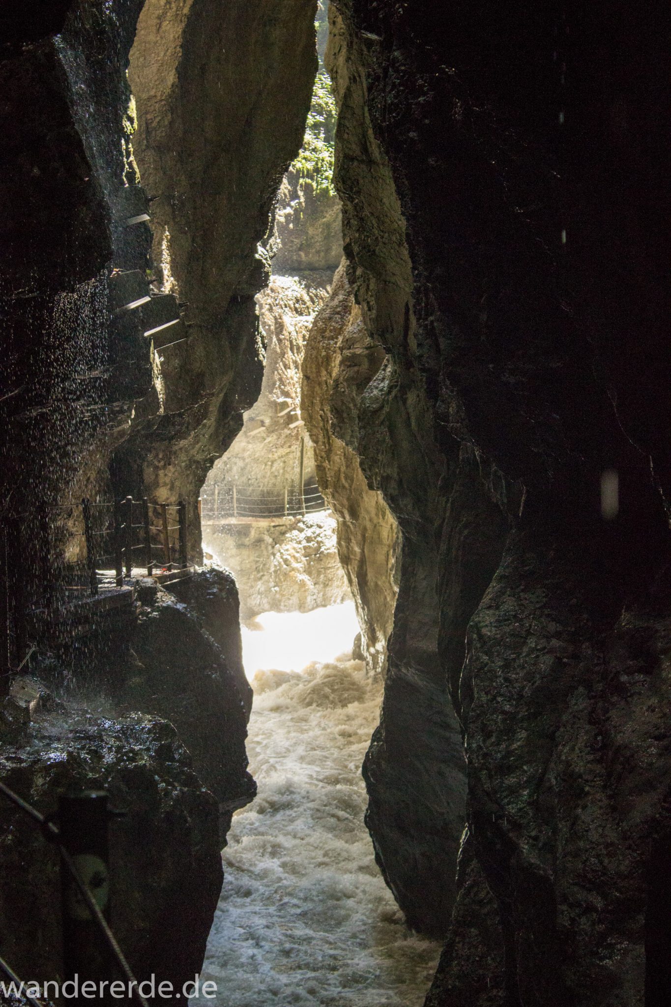 Rundwanderung Partnachklamm im Wettersteingebirge bei Garmisch-Partenkirchen, Bayern, steil aufragende Felswände, Licht strahlt durch Eingang der Klamm, gesicherter Wanderweg in den Fels gehauen, kühl und nass