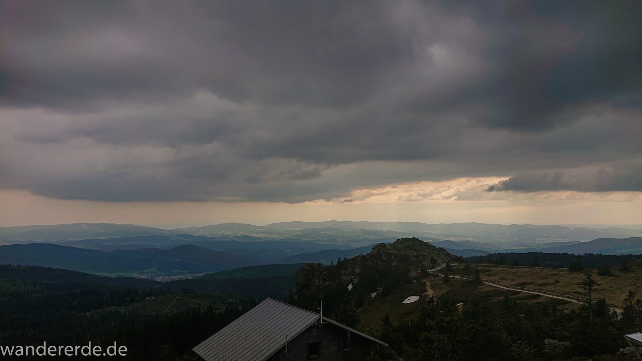 Rundwanderung zum Großen Arber im Bayerischen Wald, weite Aussicht auf riesiges Waldgebiet des bayerischen Waldes vom Berg Großer Arber, schöner und dichter Wald, Blick auf Rundweg und kleines Haus auf dem Großen Arber, Mischwald aus Laub- und Nadelbäume, Frühjahr im bayerischen Wald, sehr stimmungsvolles Licht durch dunkle Wolken und späten Tag