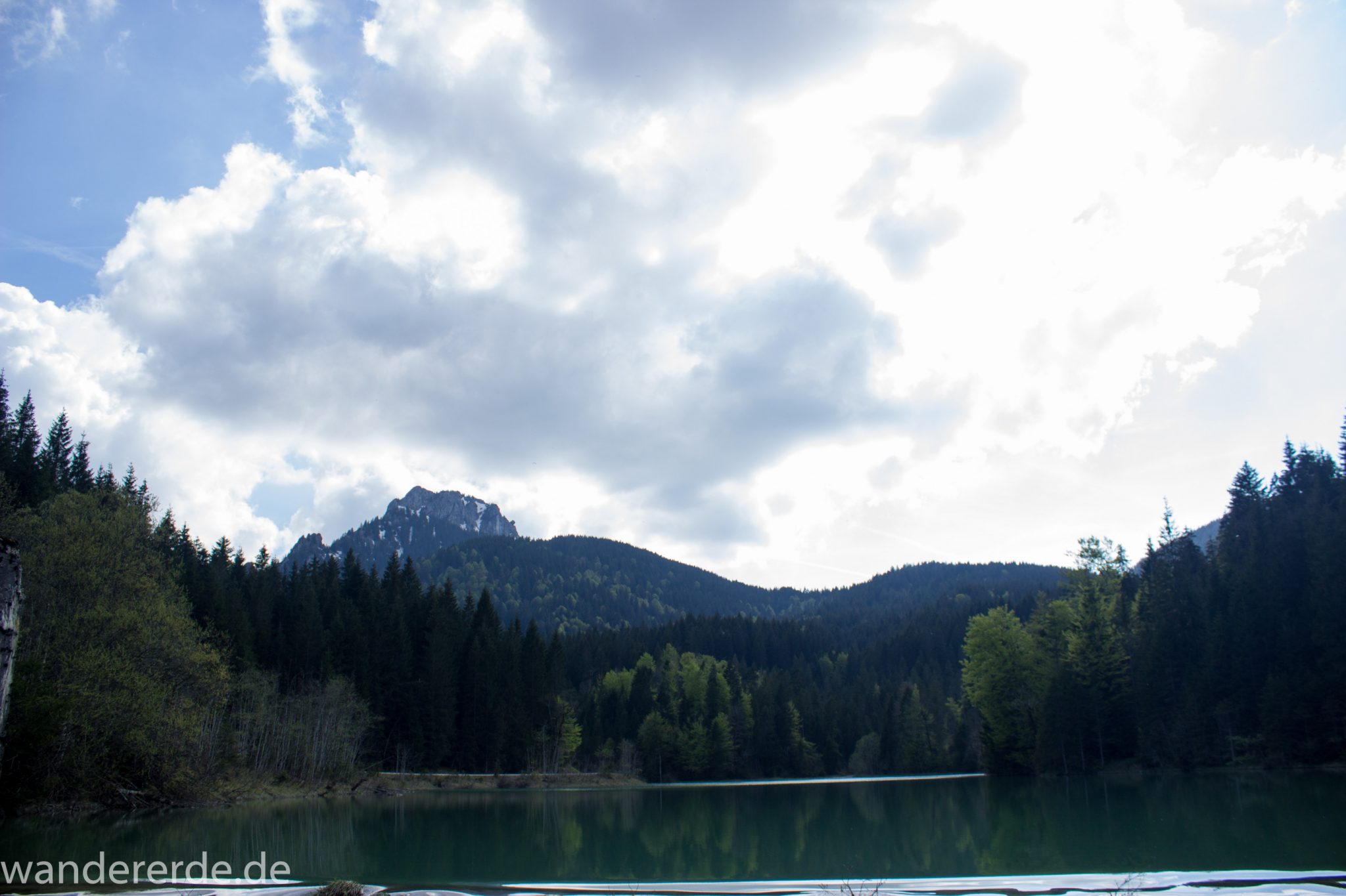 Wanderung zur Kenzenhütte in den Ammergauer Alpen, Aussicht beim Stausee auf die Berge, teils schneebedeckte Gipfel, Frühjahr in den bayerischen Alpen, dichter grüner Wald umgibt den Stausee, klares grünblaues Wasser