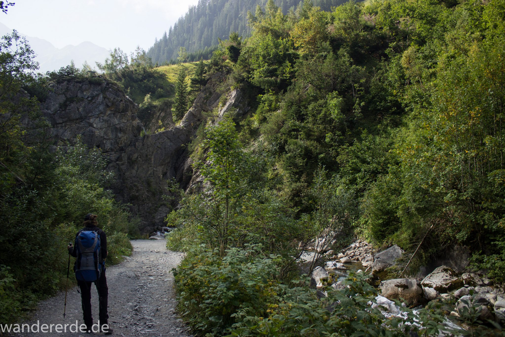 Alpenüberquerung Fernwanderweg E5 Oberstdorf Meran, 2. Etappe von Kemptner Hütte zur Memminger Hütte, Wanderer unterwegs auf schönem und abwechslungsreichem Wanderweg, Wanderpfad führt absteigend über die Obere und Untere Rossgumpenalpe in das sehr schöne Höhenbachtal mit beeindruckender Landschaft, grüne Vegetation mit Bäumen und Wiesen, idyllischer Rossgumpenbach fließt durch wolkenverhangenes Tal