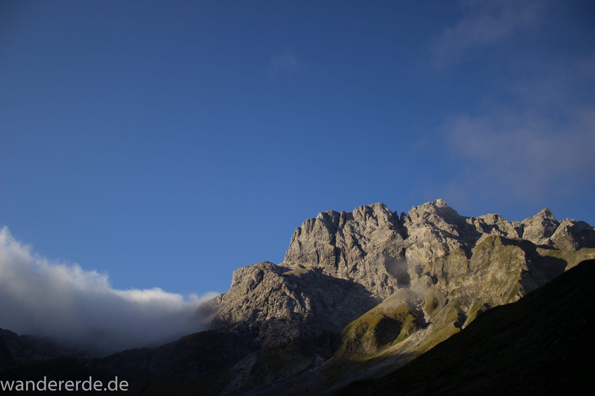 Alpenüberquerung Fernwanderweg E5 Oberstdorf Meran, 2. Etappe von Kemptner Hütte zur Memminger Hütte, kurz nach Sonnenaufgang in den Alpen bei der Kemptner Hütte, beeindruckende Berglandschaft wird in Sonnenlicht getaucht, Aussicht auf schöne Bergkette, Nebelfelder ziehen ab