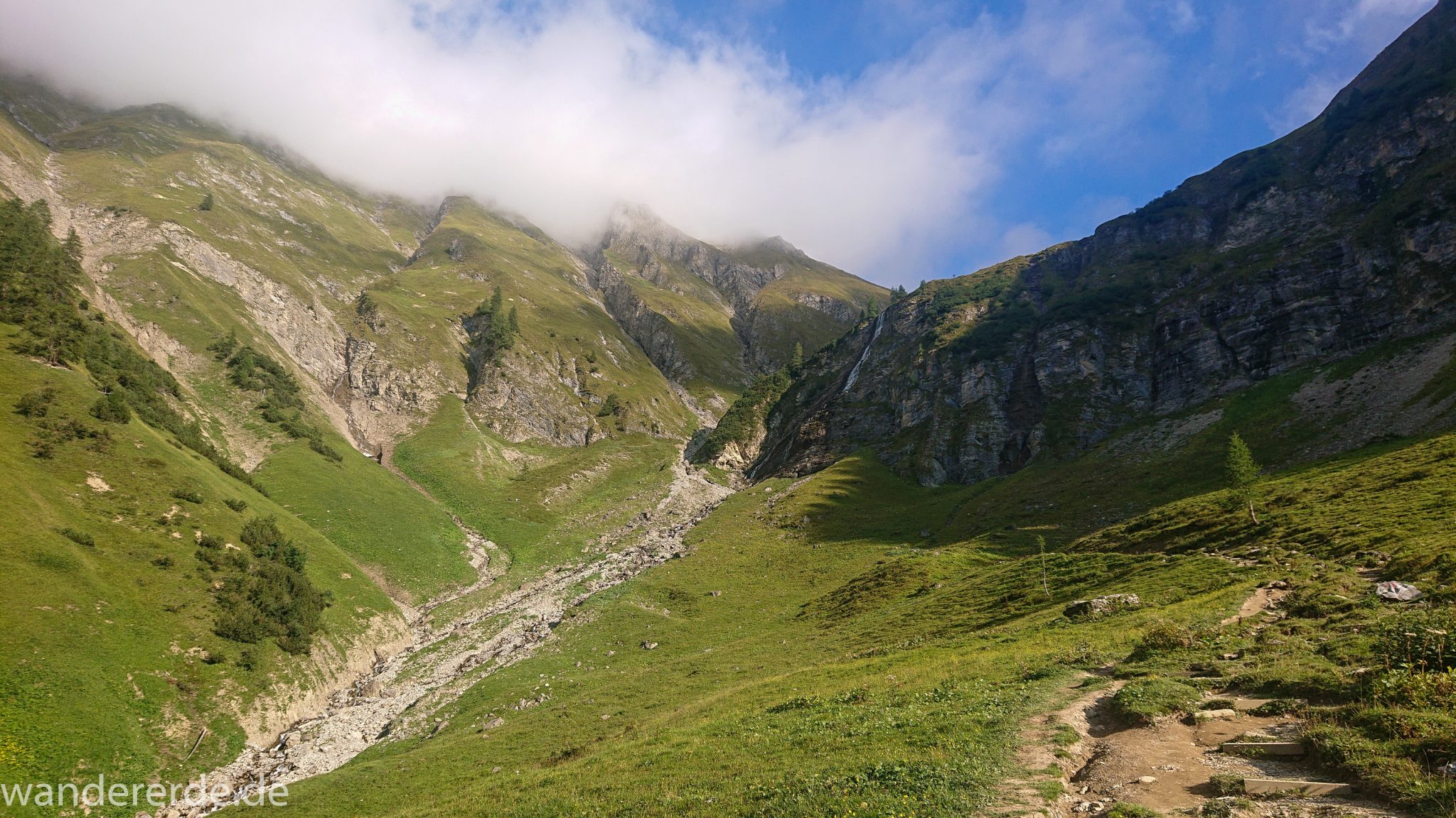 Alpenüberquerung Fernwanderweg E5 Oberstdorf Meran, 2. Etappe von Kemptner Hütte zur Memminger Hütte, schöner abwechslungsreicher und schmaler Wanderweg führt über Stock und Stein ab der Materialseilbahn der Memminger Hütte zunächst mäßig, dann steiler bergauf zur Memminger Hütte, idyllische Landschaft öffnet sich zu flacherer Ebene mit saftig grünen Wiesen, Wegverlauf zum schönen Wasserfall umgeben von beeindruckenden Bergen