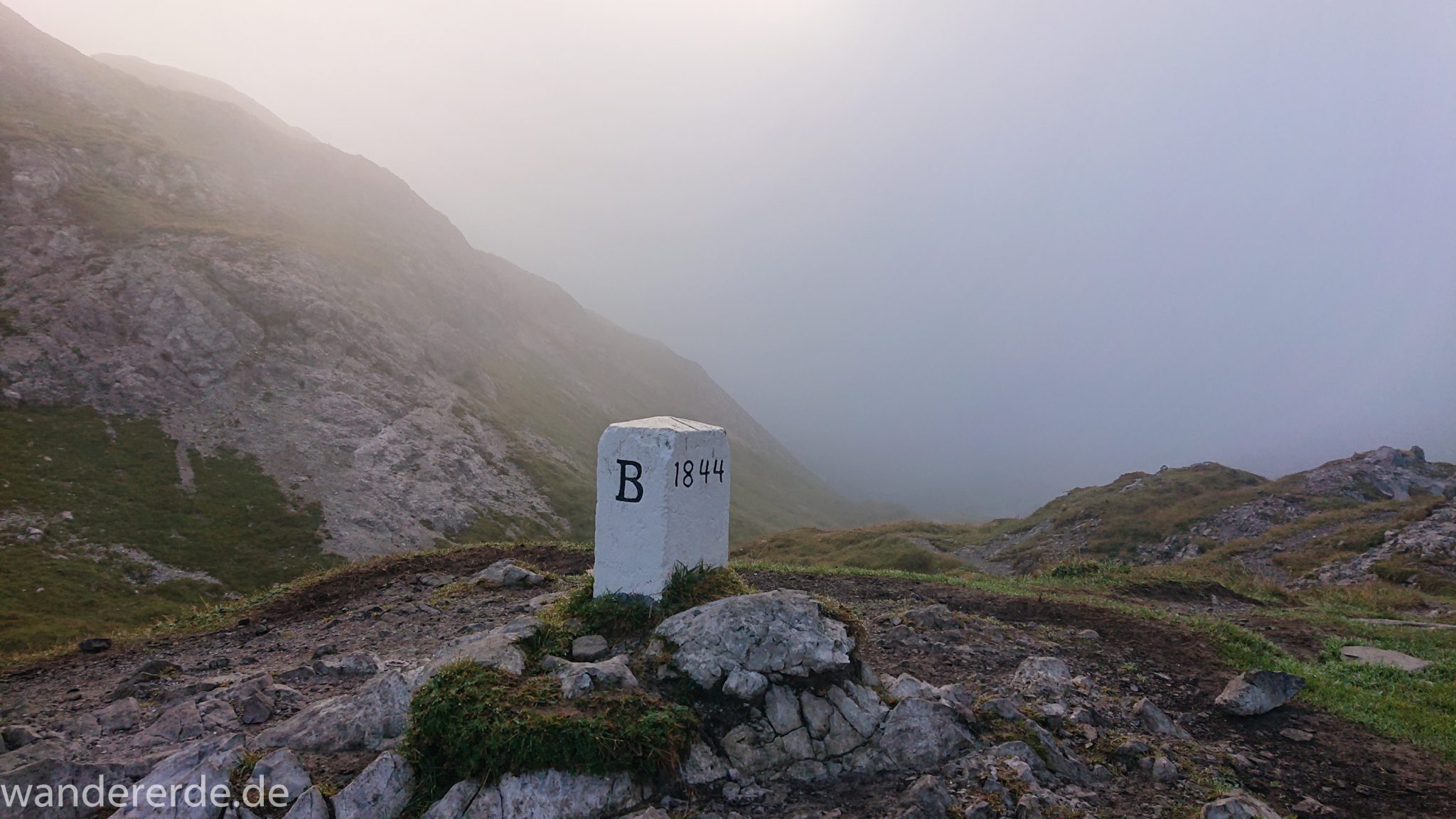 Alpenüberquerung Fernwanderweg E5 Oberstdorf Meran, 2. Etappe von Kemptner Hütte zur Memminger Hütte, Grenze von Deutschland nach Österreich, Grenzstein unweit der Kemptner Hütte beim Mädelejoch nach kurzem Aufstieg, weitere Wanderung mit eingeschränkter Sicht wegen Nebel, beeindruckende Landschaft mit Bergen