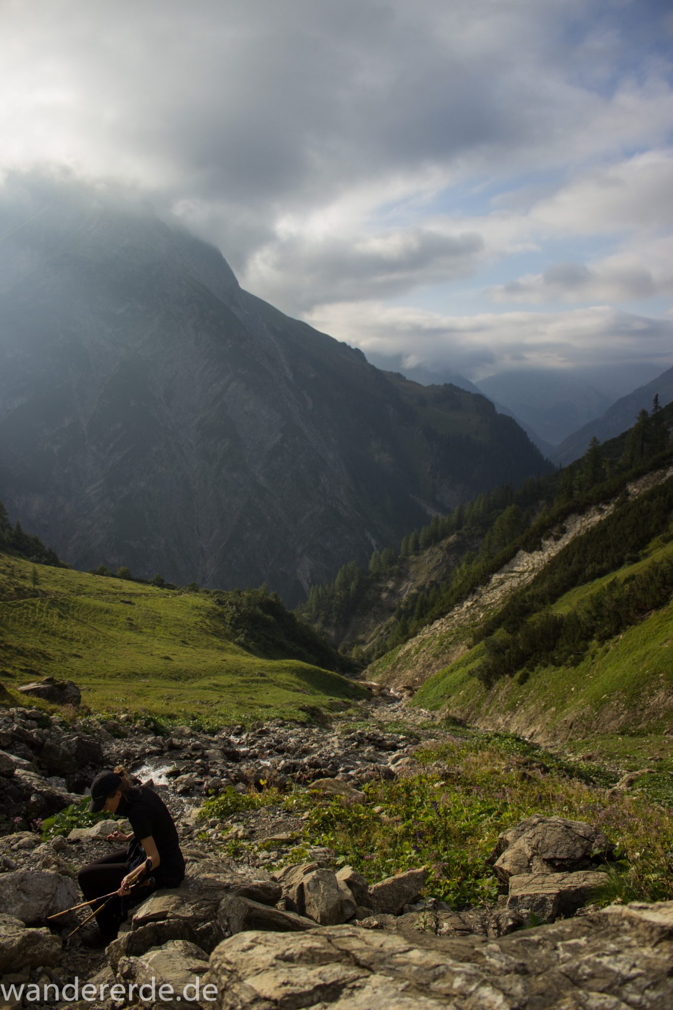 Alpenüberquerung Fernwanderweg E5 Oberstdorf Meran, 2. Etappe von Kemptner Hütte zur Memminger Hütte, schöner abwechslungsreicher und schmaler Wanderweg führt über Stock und Stein ab der Materialseilbahn der Memminger Hütte zunächst mäßig, dann steiler bergauf zur Memminger Hütte, idyllische Landschaft öffnet sich zu flacherer Ebene mit saftig grünen Wiesen und führt zum schönen Wasserfall umgeben von beeindruckenden Bergen und rundum schöner Aussicht, Wanderer macht Pause beim Wasserfall