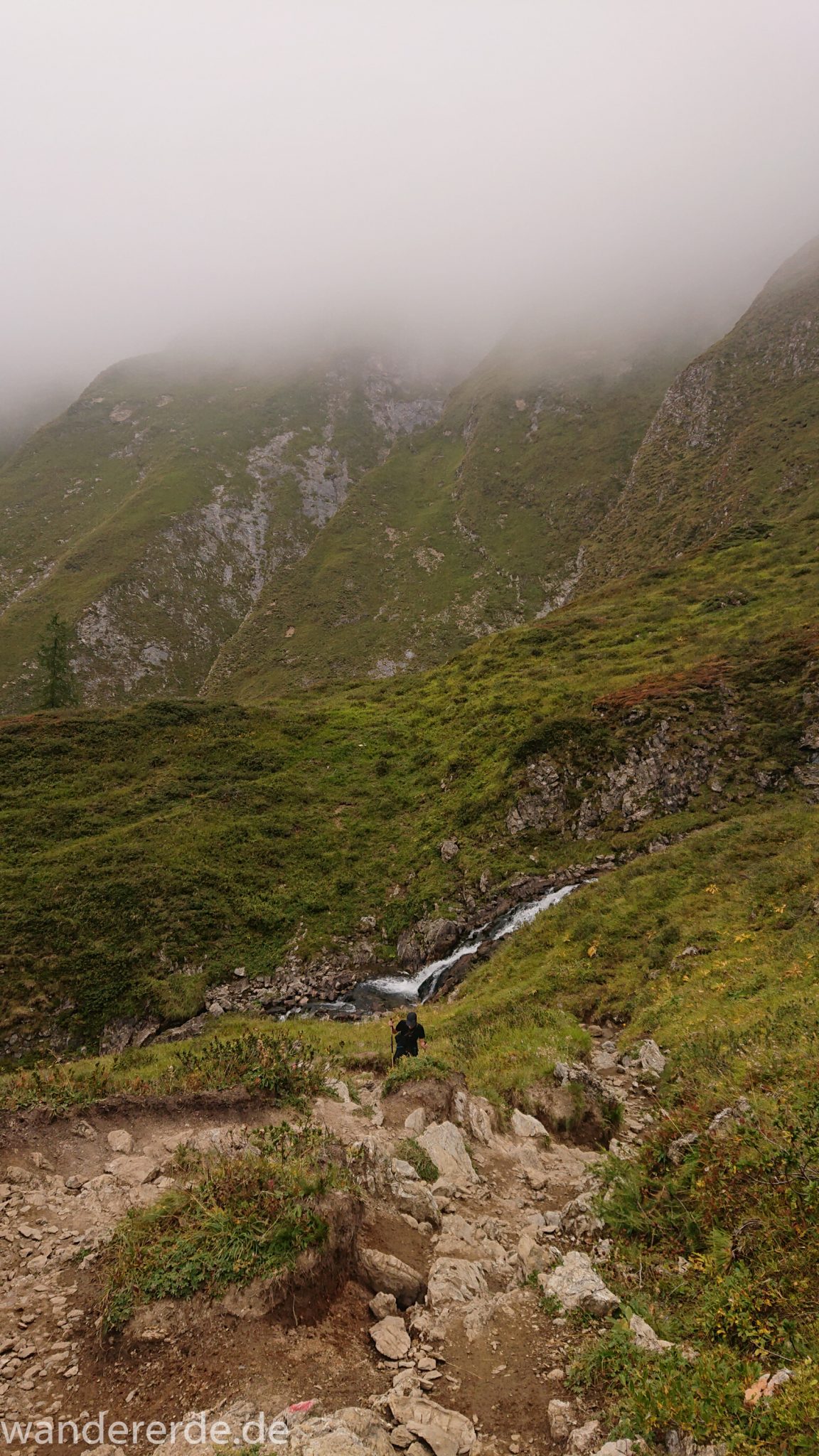 Alpenüberquerung Fernwanderweg E5 Oberstdorf Meran, 2. Etappe von Kemptner Hütte zur Memminger Hütte, schöner abwechslungsreicher und schmaler Wanderweg führt über Stock und Stein ab der Materialseilbahn der Memminger Hütte zunächst mäßig, dann steiler bergauf zur Memminger Hütte, ab schönem Wasserfall wird Wegverlauf steiler, umgeben von beeindruckenden Bergen und rundum schöner Aussicht, am späteren Nachmittag werden Berge langsam von aufziehenden Wolken verhangen, Wanderer nimmt steilen Anstieg in Angriff