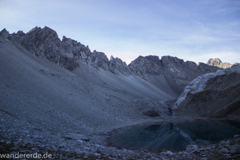 Alpenüberquerung Fernwanderweg E5 Oberstdorf Meran, 3. Etappe von Memminger Hütte zur Skihütte Zams, E5 Wanderweg führt zu Beginn der dritten Etappe ab der Memminger Hütte über steilen und ausgesetzten Wanderweg über die Seescharte, Blick auf kristallklaren Bergsee während Aufstieg zur Seescharte auf sehr schmalen Wanderweg über viel Geröll, Aussicht auf Berge der Alpen