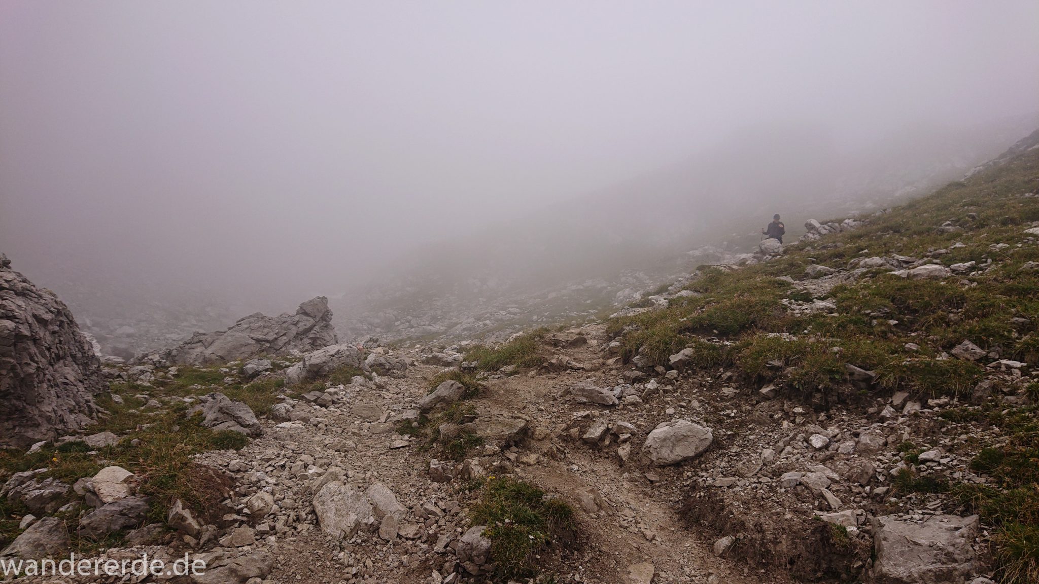 Alpenüberquerung Fernwanderweg E5 Oberstdorf Meran, 3. Etappe von Memminger Hütte zur Skihütte Zams, nach Erreichen der Seescharte folgt ein sehr langer Abstieg ins Lochbachtal Richtung Zams, Blick auf Wanderer unterwegs auf schmalem Wanderpfad mit viel Geröll, Berge und Umgebung liegen im Nebel verborgen