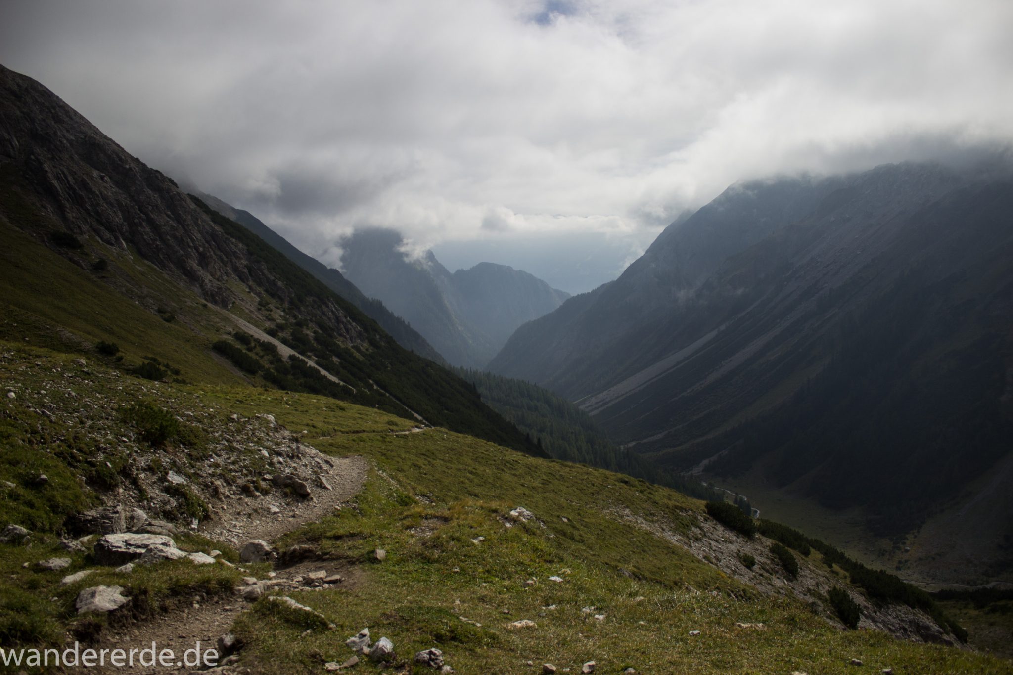Alpenüberquerung Fernwanderweg E5 Oberstdorf Meran, 3. Etappe von Memminger Hütte zur Skihütte Zams, nach Erreichen der Seescharte folgt ein sehr langer Abstieg ins Lochbachtal Richtung Zams, Aussicht auf Berge und Bergwiesen, Berge und Umgebung liegen teils im Nebel verborgen, Blick auf schmalen Wanderpfad mit viel Geröll