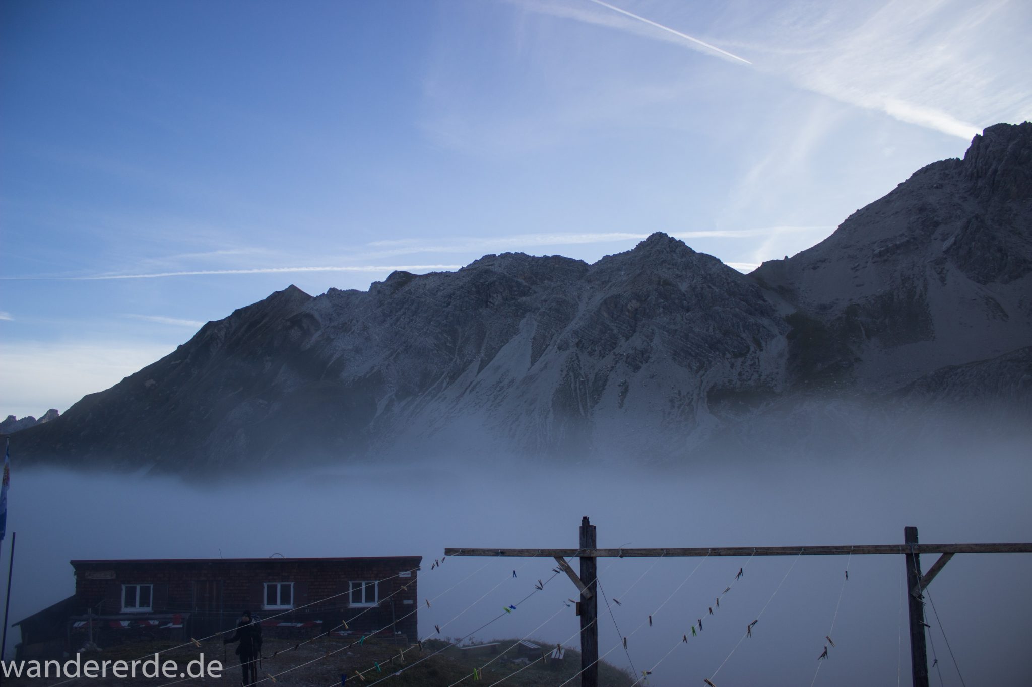 Alpenüberquerung Fernwanderweg E5 Oberstdorf Meran, 3. Etappe von Memminger Hütte zur Skihütte Zams, Berge sind am frühen Morgen noch in Nebel getaucht, aber die Sonne scheint, herrliches Wetter zum Wandern, Blick auf Nebengebäude der Memmimger Hütte, Wanderer steht davor
