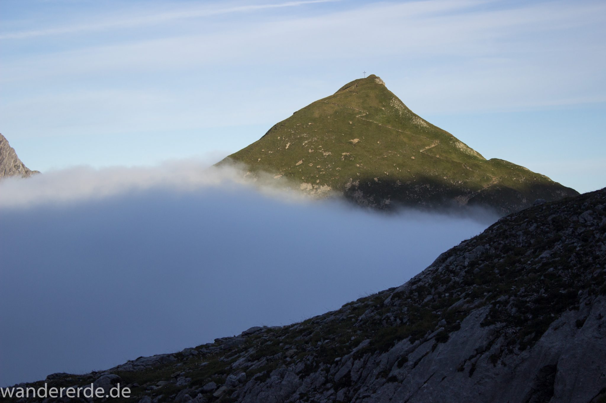 Alpenüberquerung Fernwanderweg E5 Oberstdorf Meran, 3. Etappe von Memminger Hütte zur Skihütte Zams, Berge sind am frühen Morgen noch in Nebel getaucht, aber die Sonne scheint, herrliches Wetter zum Wandern, E5 Wanderweg führt zu Beginn der dritten Etappe ab der Memminger Hütte über steilen und ausgesetzten Wanderweg über die Seescharte, Aussicht während Aufstieg auf die Seescharte auf gegenüberliegenden Berg mit Wanderweg im Sonnenlicht