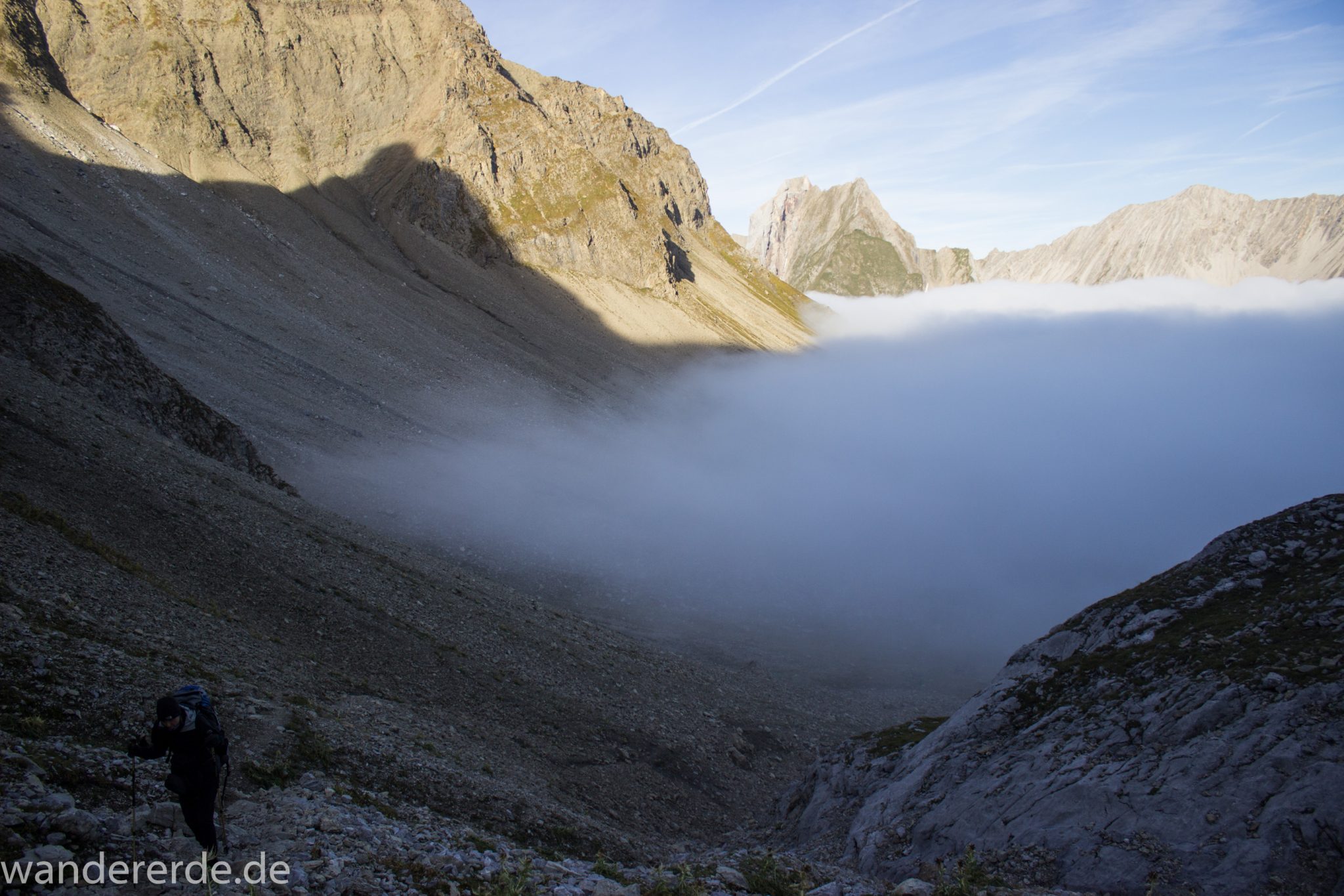 Alpenüberquerung Fernwanderweg E5 Oberstdorf Meran, 3. Etappe von Memminger Hütte zur Skihütte Zams, Berge sind am frühen Morgen noch in Nebel getaucht, aber die Sonne scheint, herrliches Wetter zum Wandern, E5 Wanderweg führt zu Beginn der dritten Etappe ab der Memminger Hütte über steilen und ausgesetzten Wanderweg über die Seescharte, Blick auf Wanderer während Aufstieg zur Seescharte auf sehr schmalem Wanderweg über viel Geröll, ringsum Aussicht auf Berge der Alpen