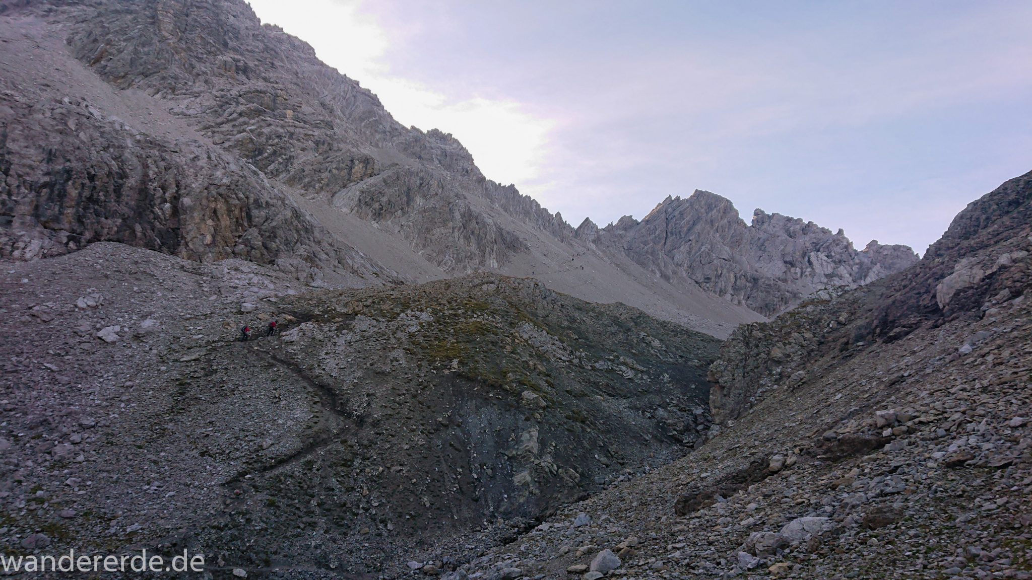 Alpenüberquerung Fernwanderweg E5 Oberstdorf Meran, 3. Etappe von Memminger Hütte zur Skihütte Zams, E5 Wanderweg führt zu Beginn der dritten Etappe ab der Memminger Hütte über steilen und ausgesetzten Wanderweg über die Seescharte, Blick auf Wanderer während Aufstieg zur Seescharte auf sehr schmalem Wanderweg über viel Geröll, Aussicht auf Berge der Alpen