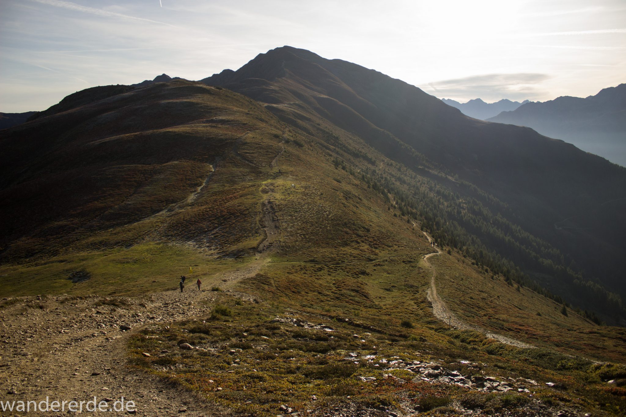 Alpenüberquerung Fernwanderweg E5 Oberstdorf Meran, 4. Etappe von Skihütte Zams zur Braunschweiger Hütte, Aussicht bei der Bergstation der Venet Bergbahn auf die Berge der Alpen, herrliches Wanderwetter bei strahlendem Sonnenschein, Wanderer sind auf schmalem Wanderweg unterwegs um über den Grat mit Kreuzjoch nach Wenns zu gehen, rechter Wanderweg Venetrundweg über Galfun Alm und Gogles Alm