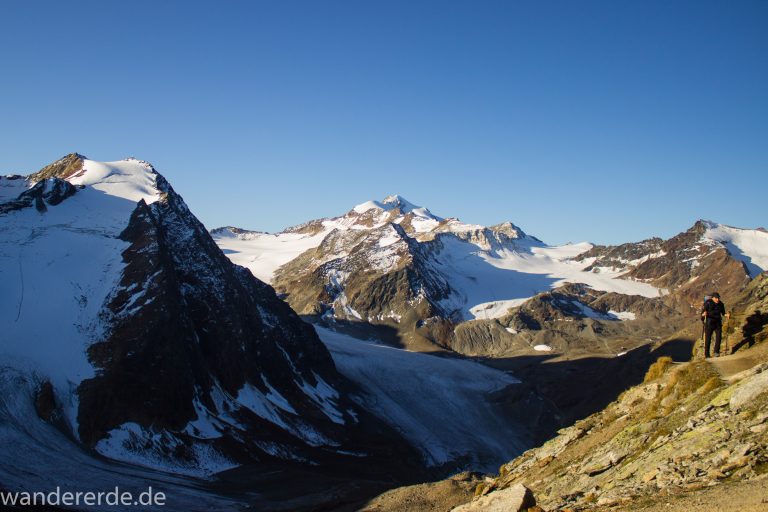 Alpenüberquerung Fernwanderweg E5 Oberstdorf Meran, 5. Etappe von Braunschweiger Hütte zur Martin-Busch-Hütte, zu Beginn der 5. Etappe steiler und schmaler Wanderweg mit viel Geröll hinauf zum Pitztaler Jöchl, Wanderer unterwegs auf Wanderpfad bei schönem Wetter, beeindruckende Berge umgeben einen, teils große Schneefelder in der Nähe der Gipfel