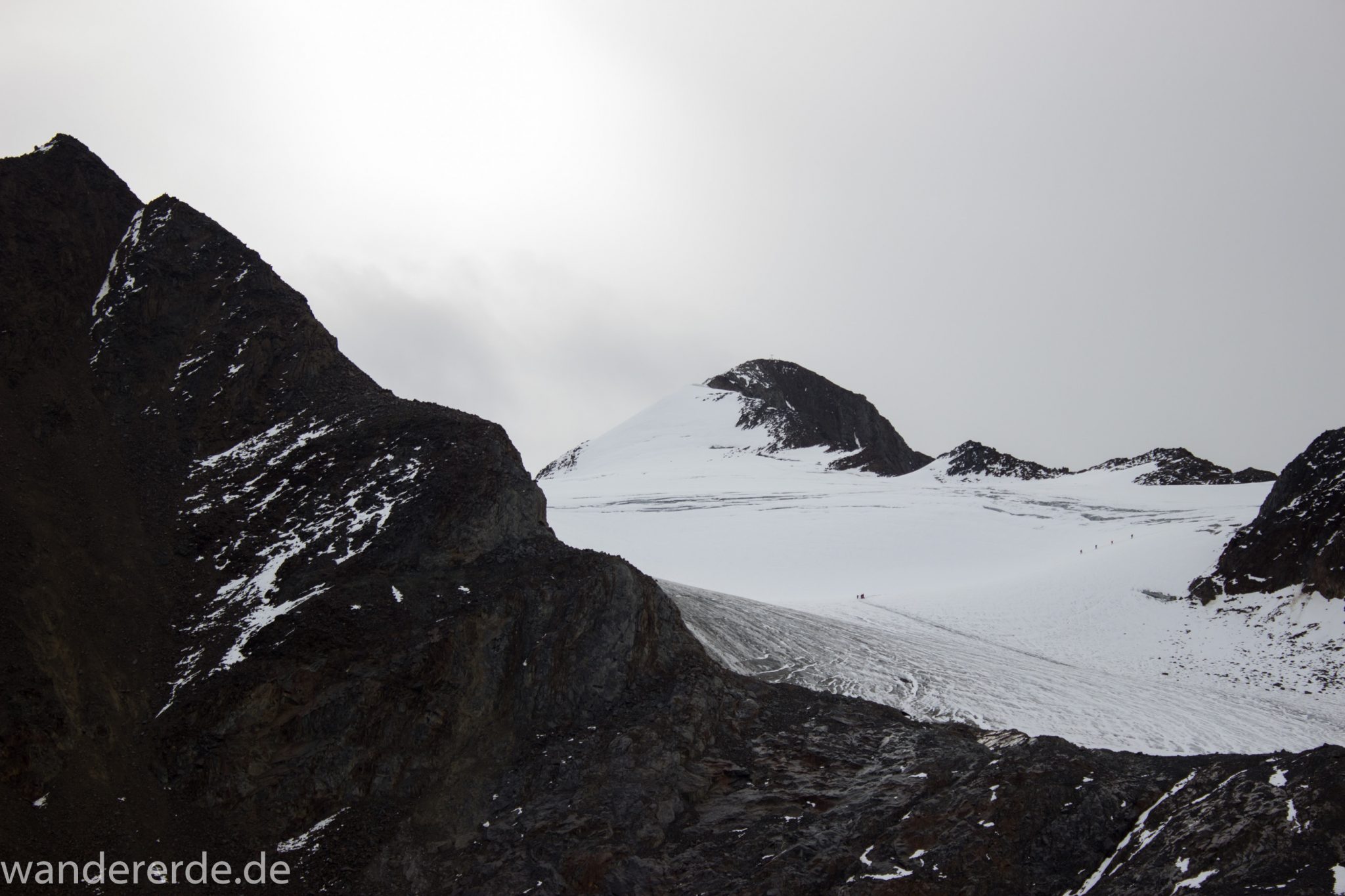 Alpenüberquerung Fernwanderweg E5 Oberstdorf Meran, 6. Etappe von Martin-Busch-Hütte nach Vernagt / Meran, die letzte Etappe der Alpenüberquerung auf dem E5 startet mit dem Aufstieg zur Similaun-Hütte, dem höchsten Punkt der gesamten Alpenüberquerung, umliegende sehr beeindruckende Bergwelt erscheint unwirklich und mystisch, Berghänge mit viel Geröll, Wanderweg verläuft steil bergauf, Blick auf Wanderer die zum Gipfel des Similaun Berges wandern über Schneefelder, nicht Teil des E5