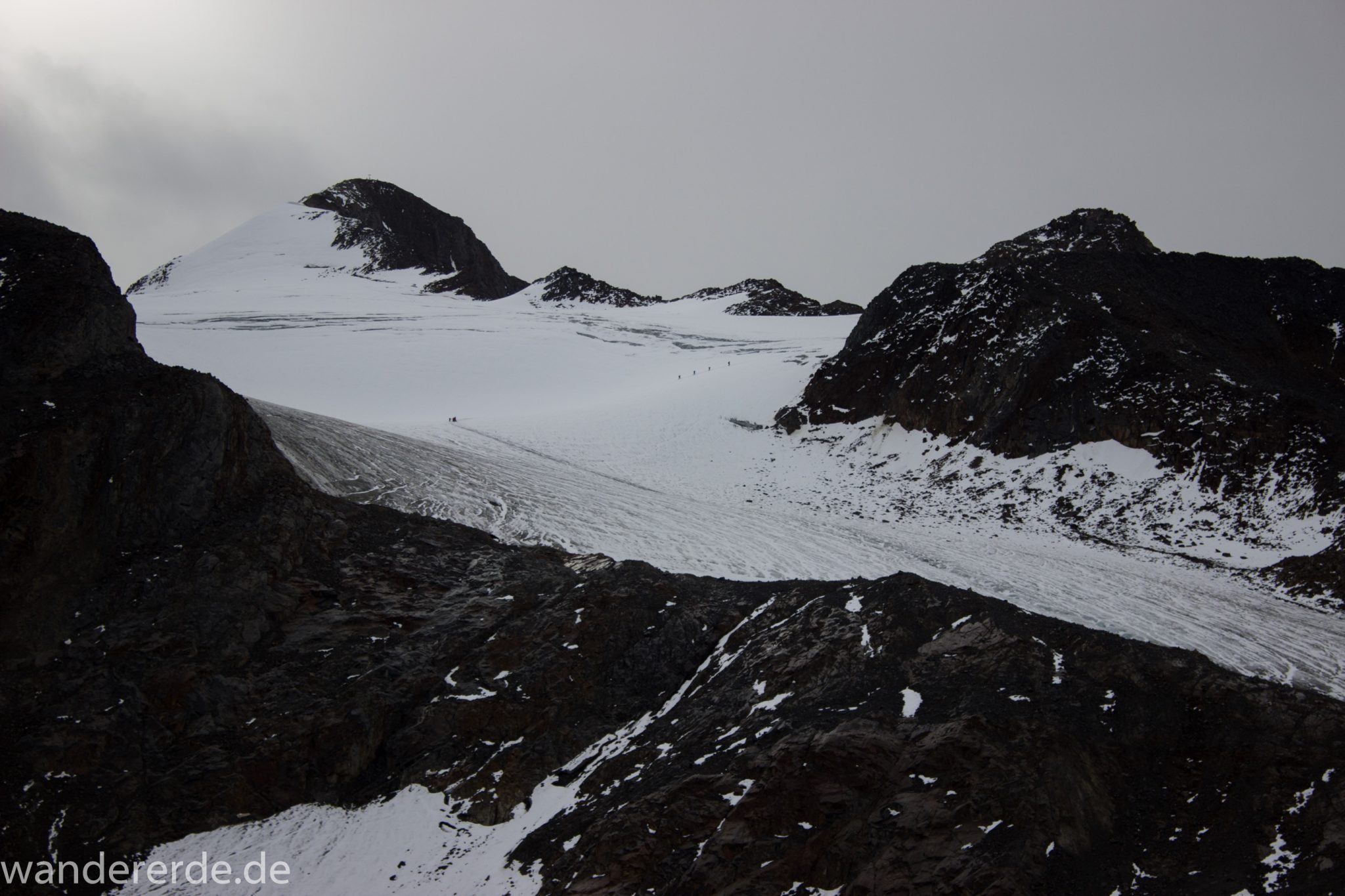 Alpenüberquerung Fernwanderweg E5 Oberstdorf Meran, 6. Etappe von Martin-Busch-Hütte nach Vernagt / Meran, die letzte Etappe der Alpenüberquerung auf dem E5 startet mit dem Aufstieg zur Similaun-Hütte, dem höchsten Punkt der gesamten Alpenüberquerung, umliegende sehr beeindruckende Bergwelt erscheint unwirklich und mystisch, Berghänge mit viel Geröll, Wanderweg verläuft steil bergauf, Blick auf Wanderer die zum Gipfel des Similaun Berges wandern über Schneefelder, nicht Teil des E5