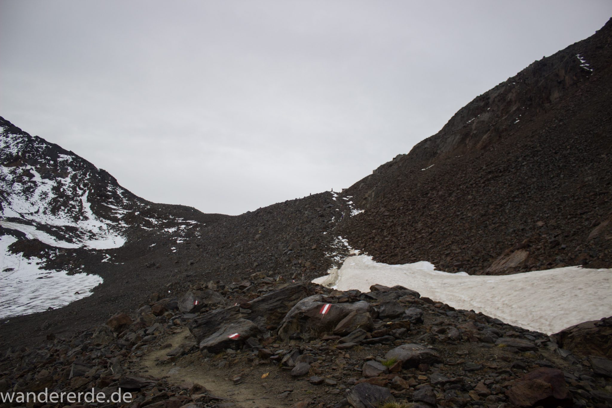Alpenüberquerung Fernwanderweg E5 Oberstdorf Meran, 6. Etappe von Martin-Busch-Hütte nach Vernagt / Meran, die letzte Etappe der Alpenüberquerung auf dem E5 startet mit dem Aufstieg zur Similaun-Hütte, dem höchsten Punkt der gesamten Alpenüberquerung, umliegende sehr beeindruckende Bergwelt erscheint unwirklich und mystisch, Berghänge mit viel Geröll, Wanderweg verläuft zunächst gering ansteigend neben einem Bach und dann steil bergauf, Blick auf Wanderer auf steilem Abschnitt mit Schneefeldern, Wegmarkierung auf Steine
