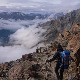 Alpenüberquerung Fernwanderweg E5 Oberstdorf Meran, 6. Etappe von Martin-Busch-Hütte nach Vernagt / Meran, die letzte Etappe der Alpenüberquerung auf dem E5 startet mit dem Aufstieg zur Similaun-Hütte, dem höchsten Punkt der gesamten Alpenüberquerung, umliegende sehr beeindruckende Bergwelt erscheint unwirklich und mystisch, Berghänge mit viel Geröll, Wanderweg verläuft nach der Similaun-Hütte steil abwärts Richtung Vernagt im Schnalstal, Wanderer während steilem Abstieg auf ausgesetztem Pfad