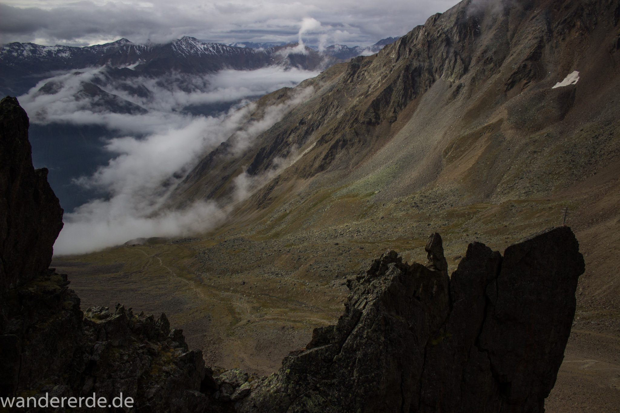 Alpenüberquerung Fernwanderweg E5 Oberstdorf Meran, 6. Etappe von Martin-Busch-Hütte nach Vernagt / Meran, nach dem Aufstieg zur Similaun-Hütte auf der letzten Etappe der Alpenüberquerung auf dem E5 verläuft der Wanderweg steil abwärts Richtung Vernagt im Schnalstal,  Blick auf Bergmassiv während Abstieg, erscheint unwirklich und mystisch, Berghänge mit viel Geröll, Wanderung mit steilem Abstieg auf ausgesetztem Pfad