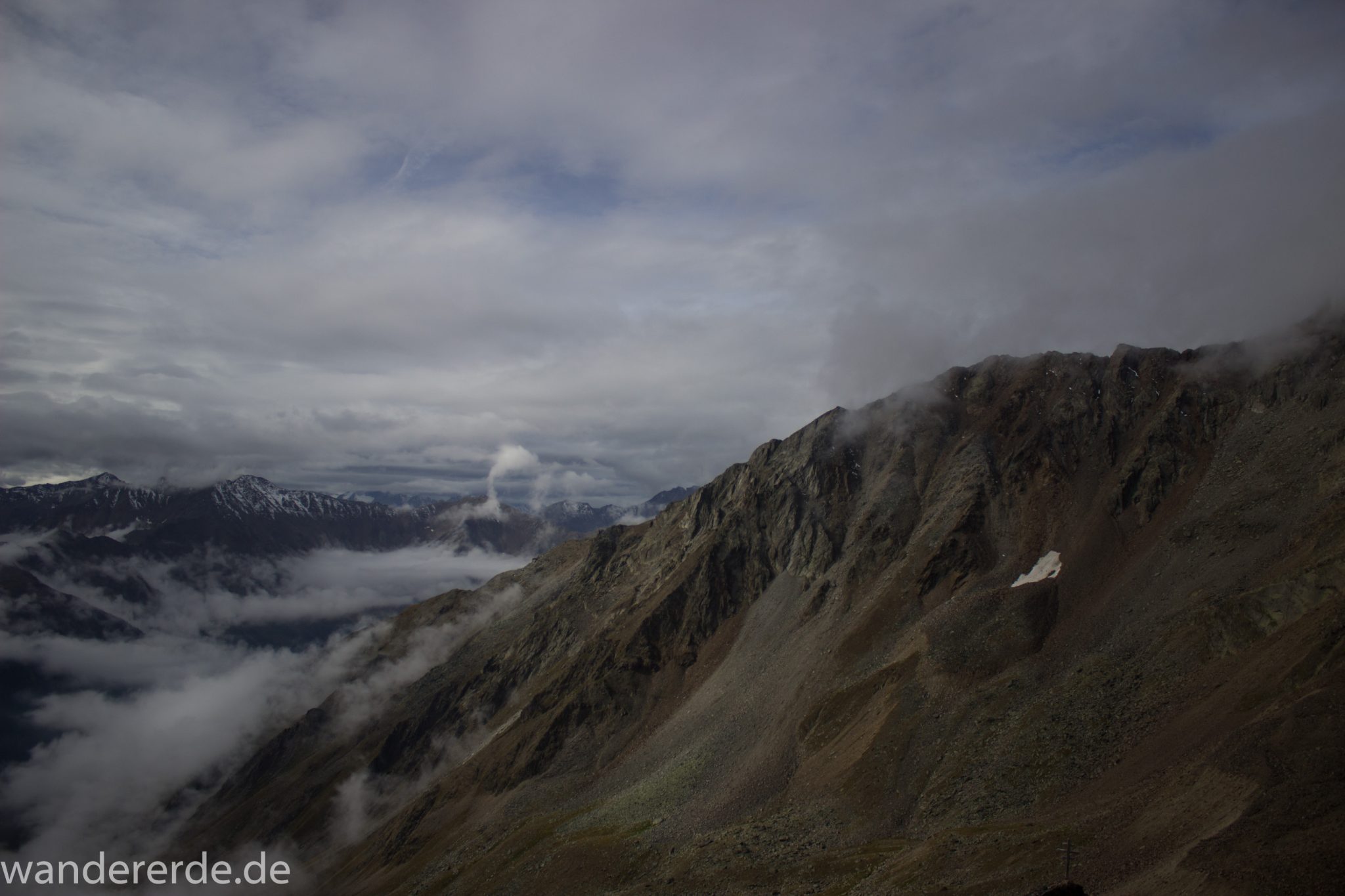 Alpenüberquerung Fernwanderweg E5 Oberstdorf Meran, 6. Etappe von Martin-Busch-Hütte nach Vernagt / Meran, nach dem Aufstieg zur Similaun-Hütte auf der letzten Etappe der Alpenüberquerung auf dem E5 verläuft der Wanderweg steil abwärts Richtung Vernagt im Schnalstal,  Blick auf Bergmassiv während Abstieg, erscheint unwirklich und mystisch, Berghänge mit viel Geröll, Wanderung mit steilem Abstieg auf ausgesetztem Pfad