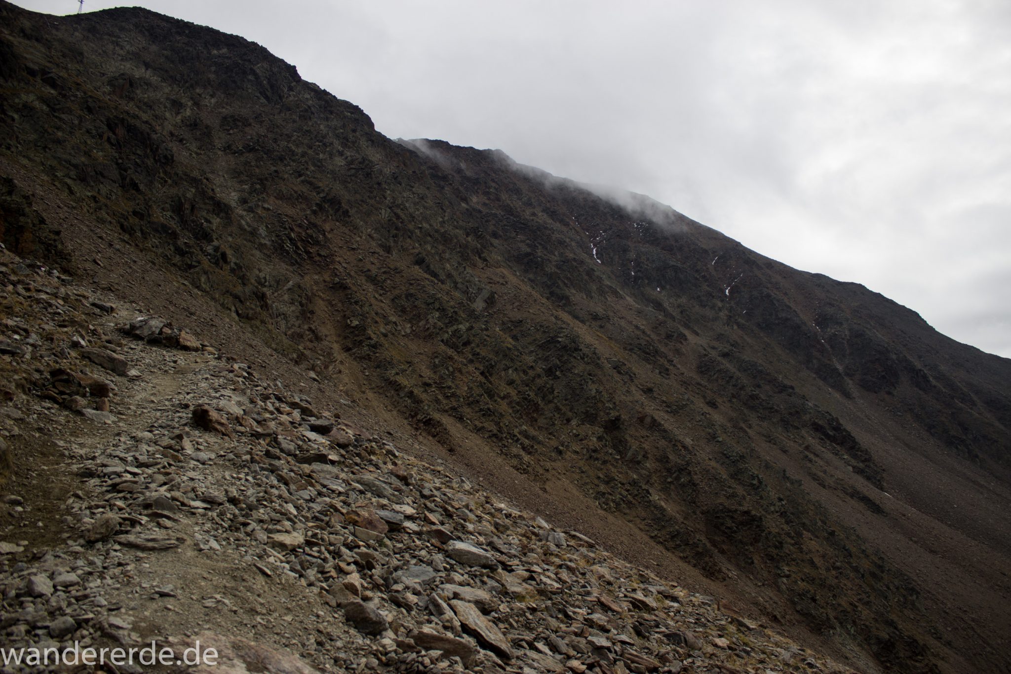 Alpenüberquerung Fernwanderweg E5 Oberstdorf Meran, 6. Etappe von Martin-Busch-Hütte nach Vernagt / Meran, nach dem Aufstieg zur Similaun-Hütte auf der letzten Etappe der Alpenüberquerung auf dem E5 verläuft der Wanderweg steil abwärts Richtung Vernagt im Schnalstal,  Blick auf Berge während Abstieg, erscheint unwirklich und mystisch, Berghänge mit viel Geröll, Wanderung mit steilem Abstieg auf ausgesetztem Pfad