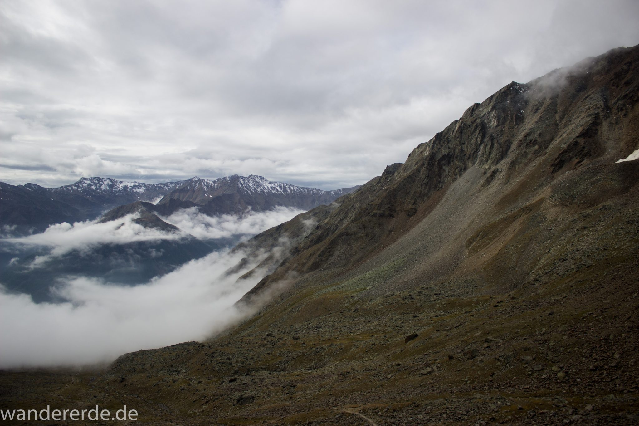 Alpenüberquerung Fernwanderweg E5 Oberstdorf Meran, 6. Etappe von Martin-Busch-Hütte nach Vernagt / Meran, nach dem Aufstieg zur Similaun-Hütte auf der letzten Etappe der Alpenüberquerung auf dem E5 verläuft der Wanderweg steil abwärts Richtung Vernagt im Schnalstal,  Blick auf Bergmassiv während Abstieg, erscheint unwirklich und mystisch, Berghänge mit viel Geröll, Wanderung mit steilem Abstieg auf ausgesetztem Pfad