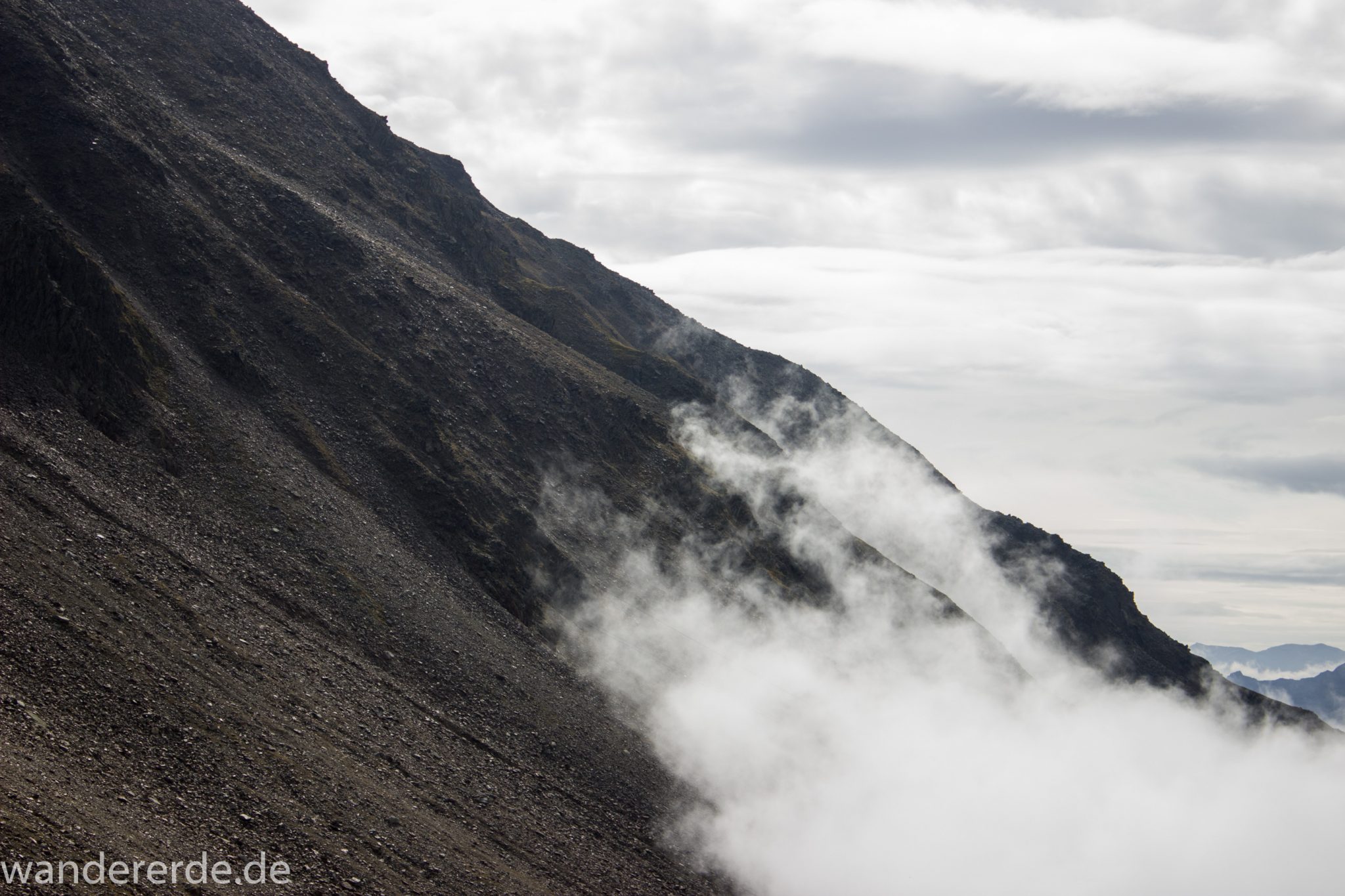 Alpenüberquerung Fernwanderweg E5 Oberstdorf Meran, 6. Etappe von Martin-Busch-Hütte nach Vernagt / Meran, nach dem Aufstieg zur Similaun-Hütte auf der letzten Etappe der Alpenüberquerung auf dem E5 verläuft der Wanderweg steil abwärts Richtung Vernagt im Schnalstal,  Blick auf Berge während Abstieg, erscheint unwirklich und mystisch, Berghänge mit viel Geröll, Wanderung mit steilem Abstieg auf ausgesetztem Pfad
