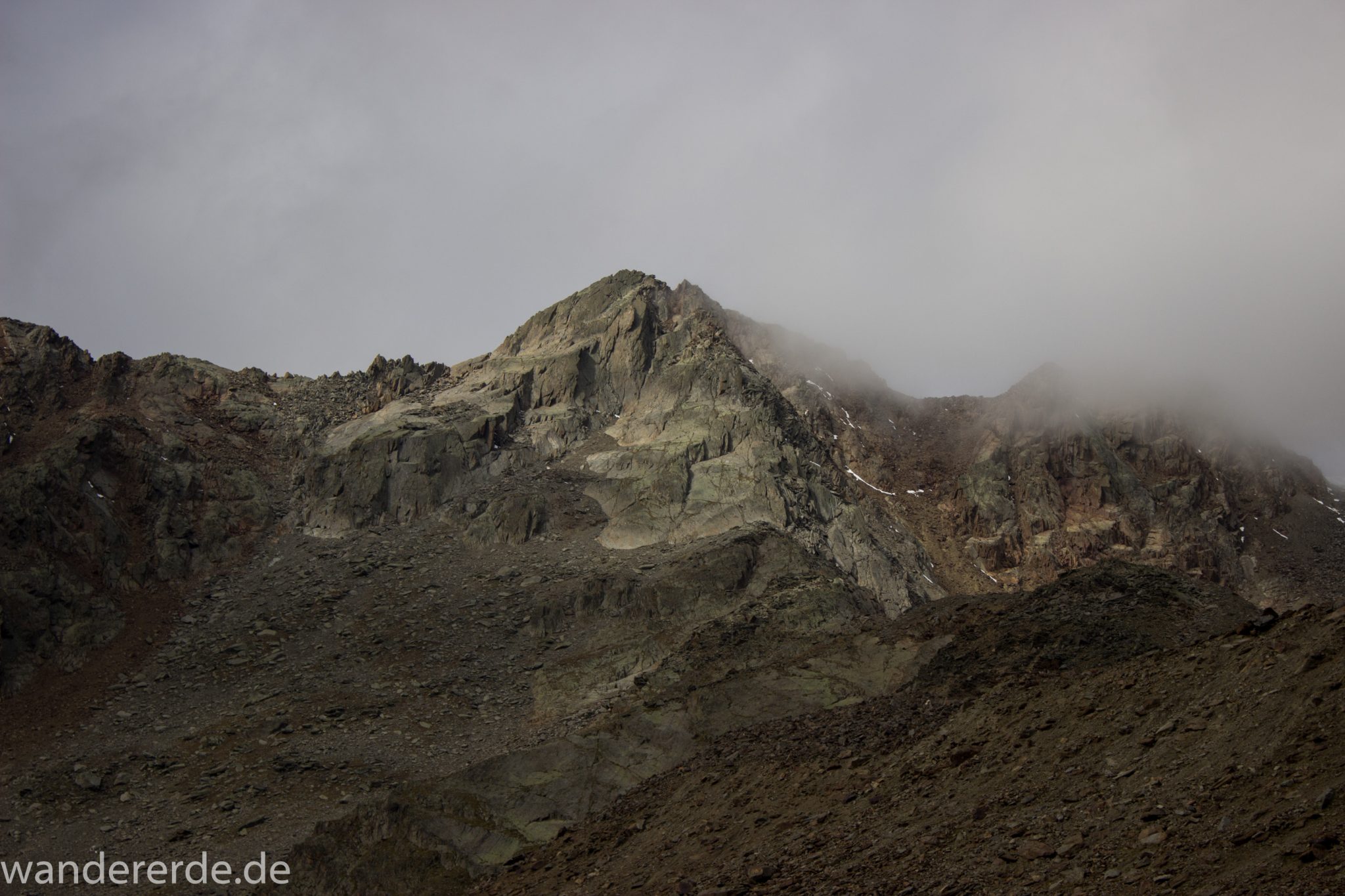 Alpenüberquerung Fernwanderweg E5 Oberstdorf Meran, 6. Etappe von Martin-Busch-Hütte nach Vernagt / Meran, nach dem Aufstieg zur Similaun-Hütte auf der letzten Etappe der Alpenüberquerung auf dem E5 verläuft der Wanderweg steil abwärts Richtung Vernagt im Schnalstal,  Blick auf Berge während Abstieg, erscheint unwirklich und mystisch, Berghänge mit viel Geröll, Wanderung mit steilem Abstieg auf ausgesetztem Pfad