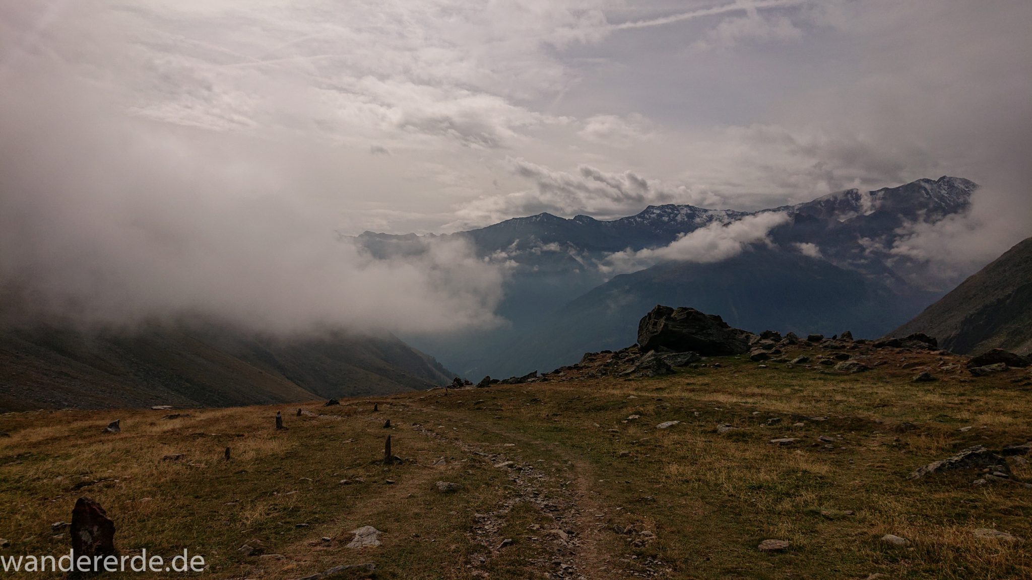 Alpenüberquerung Fernwanderweg E5 Oberstdorf Meran, 6. Etappe von Martin-Busch-Hütte nach Vernagt / Meran, nach dem Aufstieg zur Similaun-Hütte auf der letzten Etappe der Alpenüberquerung auf dem E5 verläuft der Wanderweg steil abwärts Richtung Vernagt im Schnalstal,  Blick auf Bergmassiv während Abstieg, Sicht teils durch Wolken verhindert, erscheint unwirklich und mystisch, Wanderung mit steilem Abstieg auf ausgesetztem Pfad