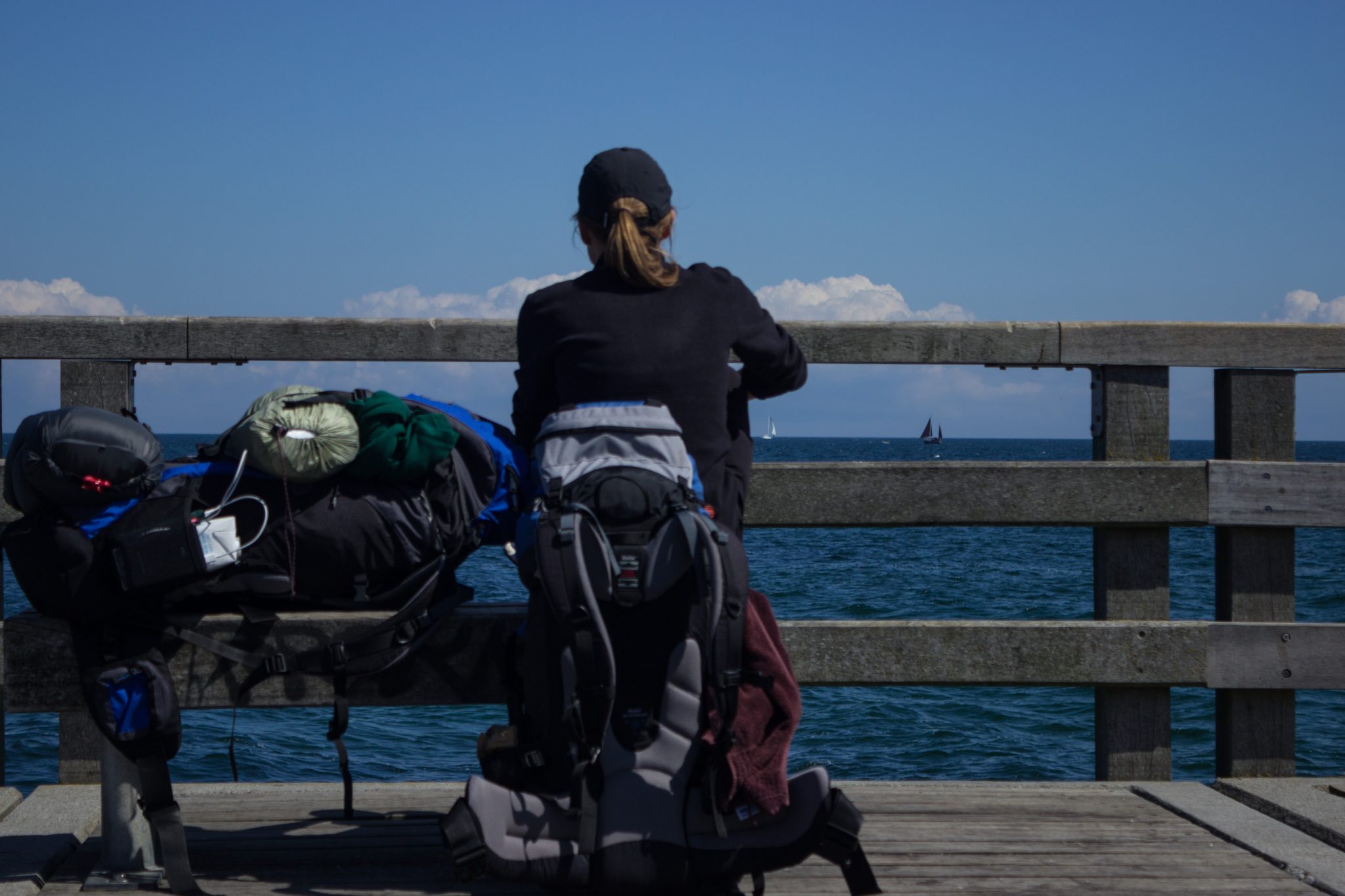 Wandern an der Ostsee von Kühlungsborn nach Börgerende auf dem E9, dritte Etappe des Wanderwegs an der Ostseeküste von Wismar nach Zingst, Blick von der Seebrücke in Kühlungsborn Richtung unendlicher Ostsee, strahlend blauer Himmel im Sommer, Wanderer mit großen Rucksäcken machen wohlverdiente Pause und genießen die Aussicht
