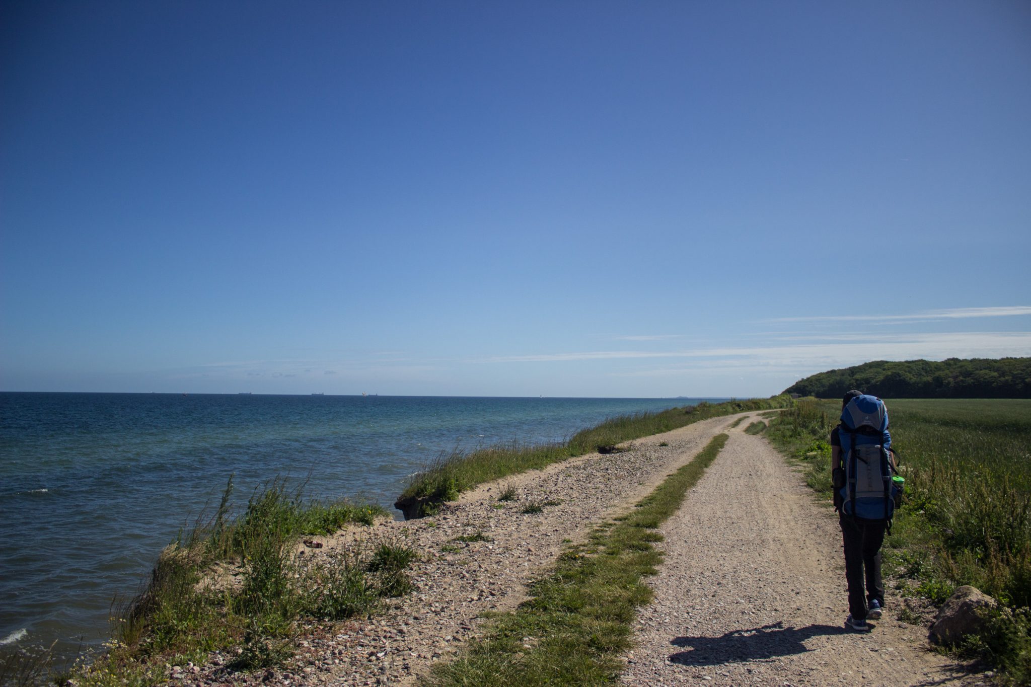 Wandern an der Ostsee von Börgerende nach Markgrafenheide auf dem E9, vierte Etappe des Wanderwegs an der Ostseeküste von Wismar nach Zingst, Wanderer mit großem Rucksack auf Wanderweg unterwegs, Wander- und Radweg bei Nienhagen offiziell gesperrt, aber niemand hält sich daran und es ist auch keine Absperrung vorhanden, durch den kühlen Ostseewind ist es trotz Sonne angenehm und die weiten Meerblicke sind schön