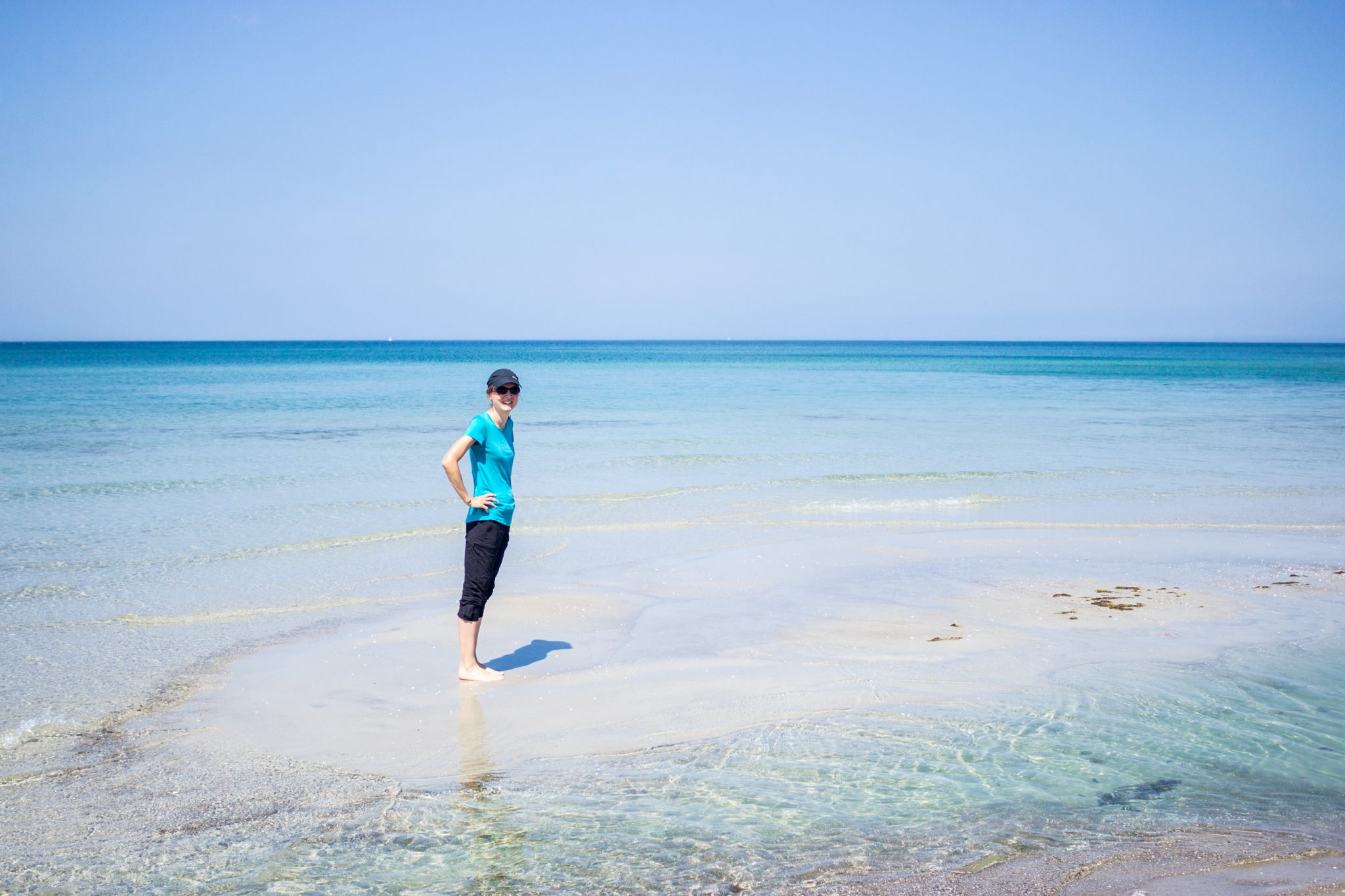 Wandern an der Ostsee von Ahrenshoop nach Zingst auf dem E9, siebte Etappe des Wanderwegs an der Ostseeküste von Wismar nach Zingst, Wanderer steht an langem, weißem Sandstrand in Ahrenshoop an der Ostsee, schönes, sauberes Meer mit klarem Wasser, kleine Wellen brechen sanft am Ufer, wolkenloser Himmel, Bild könnte auch in der Karibik entstanden sein