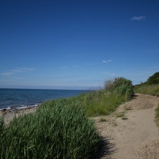 Wandern an der Ostsee vom Salzhaff nach Kühlungsborn auf dem E9 Fernwanderweg, zweite Etappe des Wanderwegs an der Ostseeküste von Wismar nach Zingst, Blick auf die schöne Ostsee im Sommer, fast menschenleerer Strand, sandiger Wanderweg mit direktem Meerblick