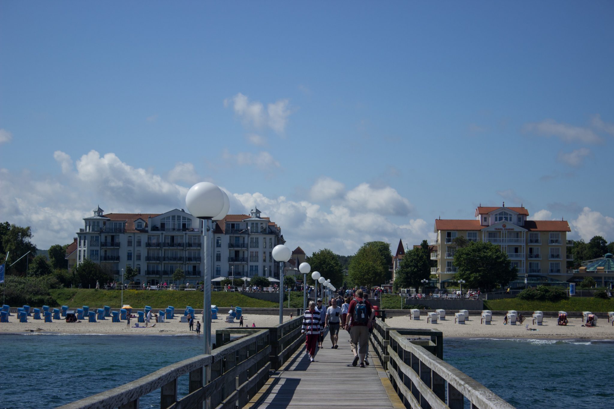 Wandern an der Ostsee von Kühlungsborn nach Börgerende auf dem E9, dritte Etappe des Wanderwegs an der Ostseeküste von Wismar nach Zingst, Blick auf die Seebrücke in Kühlungsborn Richtung Ort und Strand mit Strandkörben, Spaziergänger auf der Seebrücke, strahlend blauer Himmel im Sommer