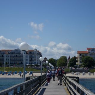 Wandern an der Ostsee von Kühlungsborn nach Börgerende auf dem E9, dritte Etappe des Wanderwegs an der Ostseeküste von Wismar nach Zingst, Blick auf die Seebrücke in Kühlungsborn Richtung Ort und Strand mit Strandkörben, Spaziergänger auf der Seebrücke, strahlend blauer Himmel im Sommer