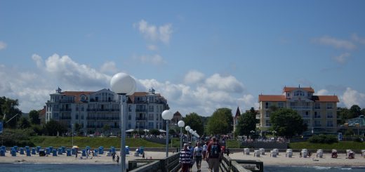 Wandern an der Ostsee von Kühlungsborn nach Börgerende auf dem E9, dritte Etappe des Wanderwegs an der Ostseeküste von Wismar nach Zingst, Blick auf die Seebrücke in Kühlungsborn Richtung Ort und Strand mit Strandkörben, Spaziergänger auf der Seebrücke, strahlend blauer Himmel im Sommer