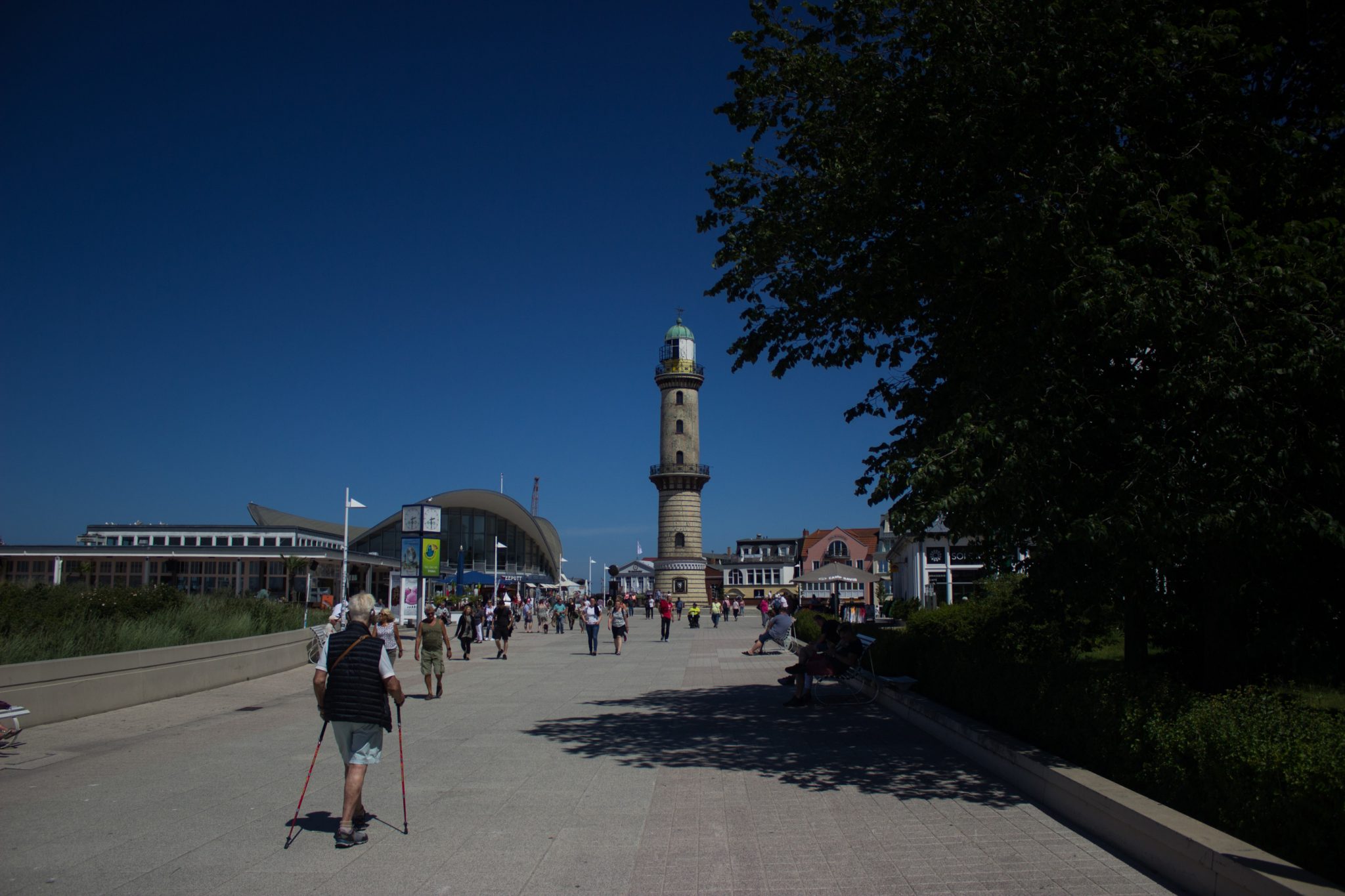 Wandern an der Ostsee von Börgerende nach Markgrafenheide auf dem E9, vierte Etappe des Wanderwegs an der Ostseeküste von Wismar nach Zingst, bekannter Leuchtturm im Zentrum des Ostseebades Warnemünde, Wanderweg führt an der langen und sehr breiten Promenade durch Warnemünde, warm im Sommer, da kein Schatten, viele Spaziergänger unterwegs