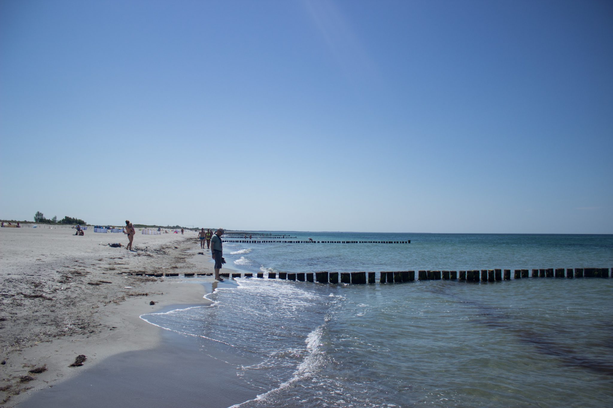 Wandern an der Ostsee von Dierhagen nach Ahrenshoop auf dem E9, sechste Etappe des Wanderwegs an der Ostseeküste von Wismar nach Zingst, am Strand an der Ostsee wandern wir weiter Richtung Ort Wustrow, traumhaft schöne Aussicht auf das Meer, Ostsee mit sauberem klarem Wasser, kleine Wellen brechen am Ufer, Spaziergänger am Strand, wolkenloser Himmel und Sonnenschein im Sommer