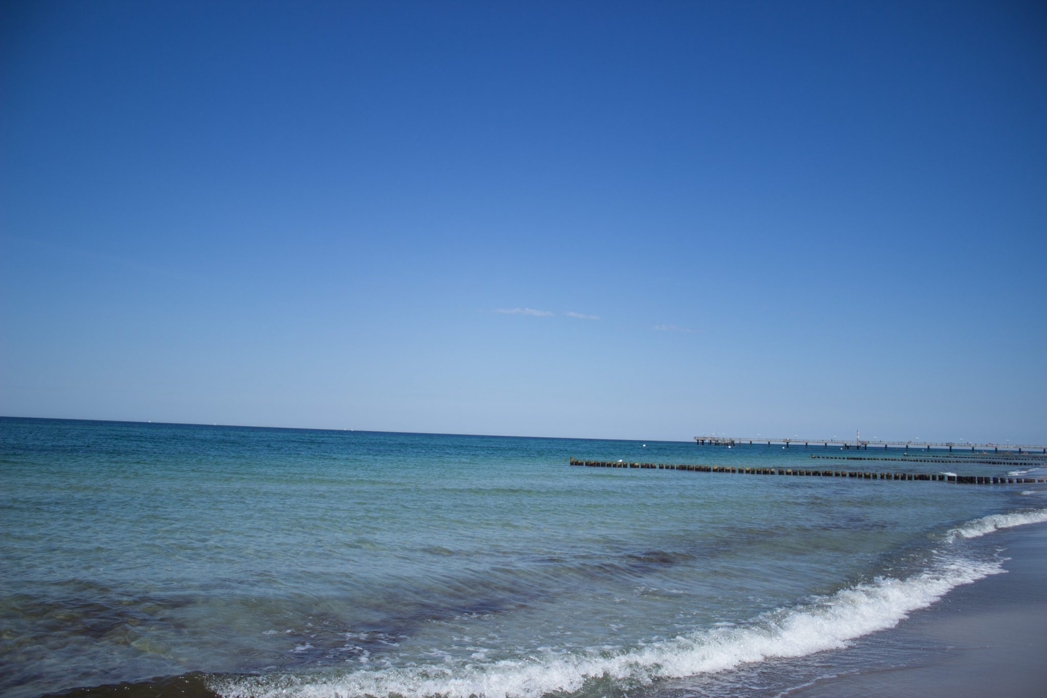 Wandern an der Ostsee von Dierhagen nach Ahrenshoop auf dem E9, sechste Etappe des Wanderwegs an der Ostseeküste von Wismar nach Zingst, am Strand an der Ostsee wandern wir weiter Richtung Ort Wustrow, traumhaft schöne Aussicht auf das Meer, Ostsee mit sauberem klarem Wasser, kleine Wellen brechen am Ufer, wolkenloser Himmel, Sonnenschein im Sommer