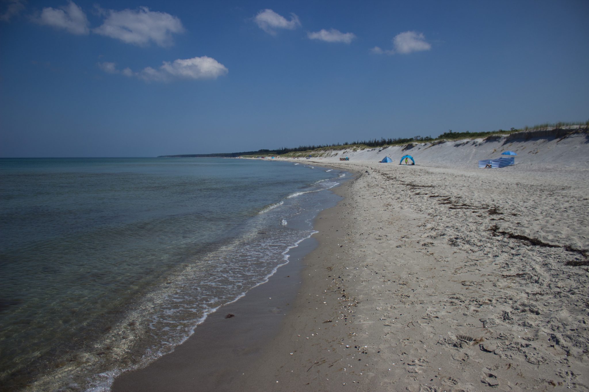 Wandern an der Ostsee von Ahrenshoop nach Zingst auf dem E9, siebte Etappe des Wanderwegs an der Ostseeküste von Wismar nach Zingst, langer, weißer Sandstrand in Ahrenshoop an der Ostsee, schönes, sauberes Meer mit klarem Wasser, kleine Wellen brechen sanft am Ufer, weitläufiger Strand