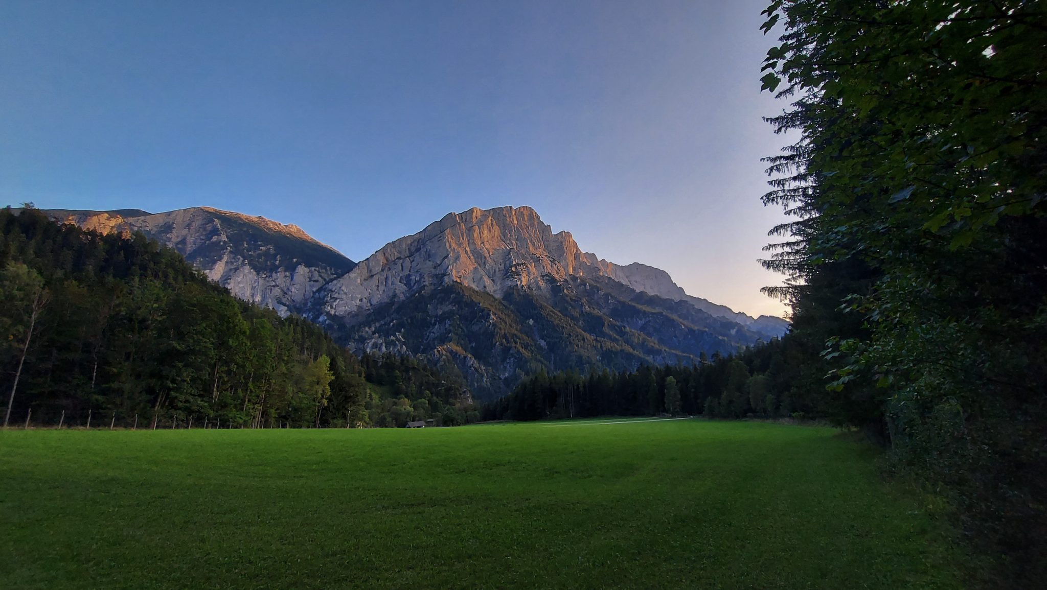Wandern zur Ennstaler Hütte im Nationalpark Gesäuse im Bundesland Steiermark in Österreich, Wanderweg in den Ennstaler Alpen ab Parkplatz Gstatterboden, Blick vom Wanderweg beim Rückweg über die Hochscheibenalm von der Ennstaler Hütte, saftig grüne Wiesen und Vegetation und Aussicht auf beeindruckende Berge in der Ferne, untergehende Sonne lässt schönes Licht entstehen